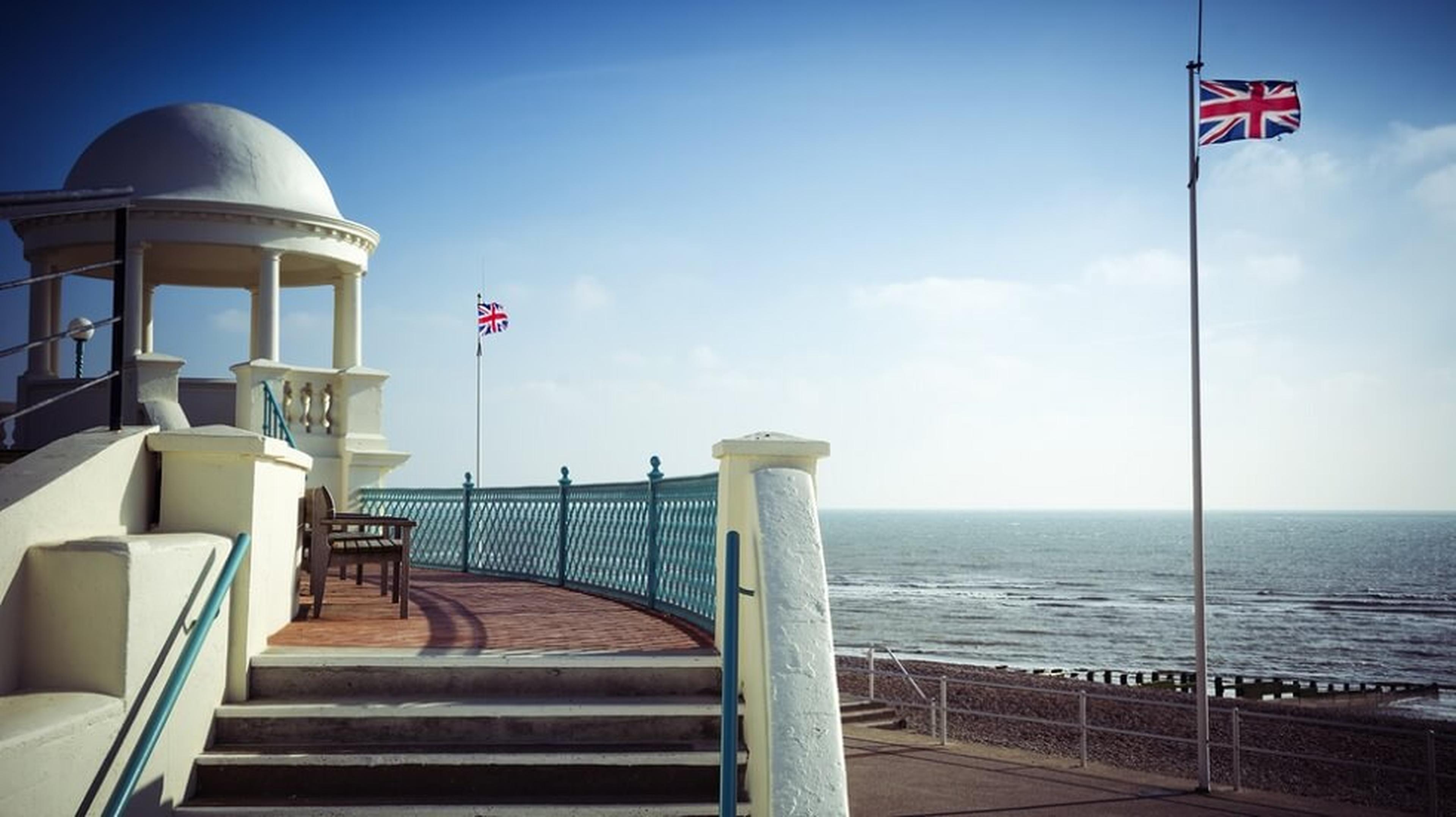 Coastal promenade with a domed gazebo, British flags, and a view of the sea