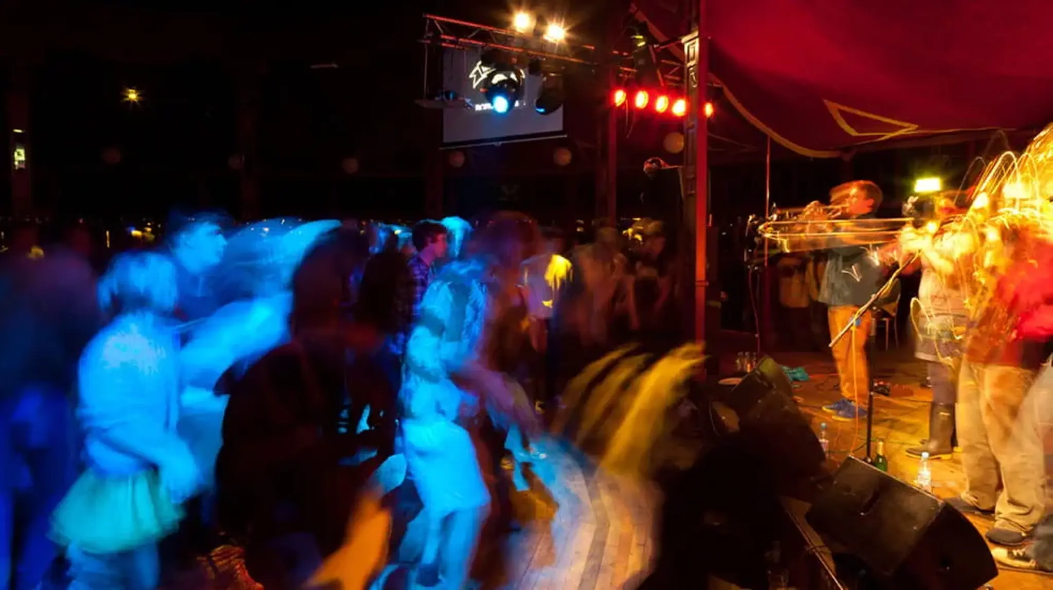 A dimly lit concert scene with a live brass band and a crowd dancing
