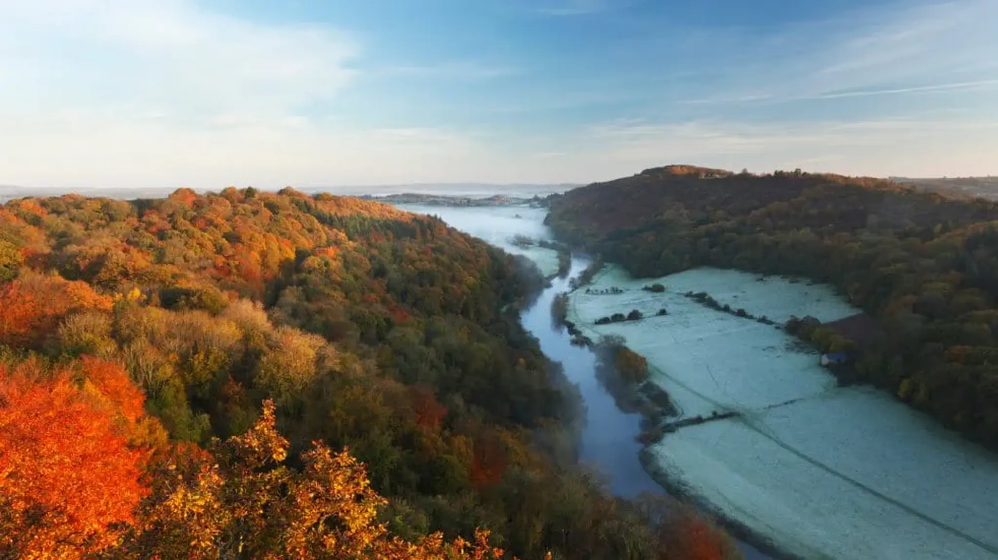 Aerial view of a river winding through autumn-coloured forests and frosty fields