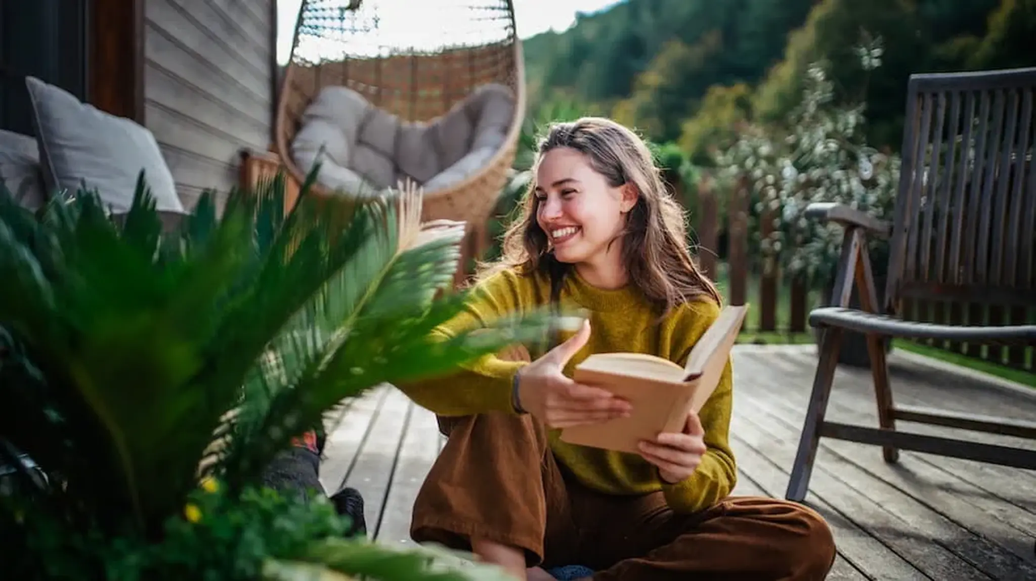 Woman sitting on a wooden deck, smiling and holding an open book