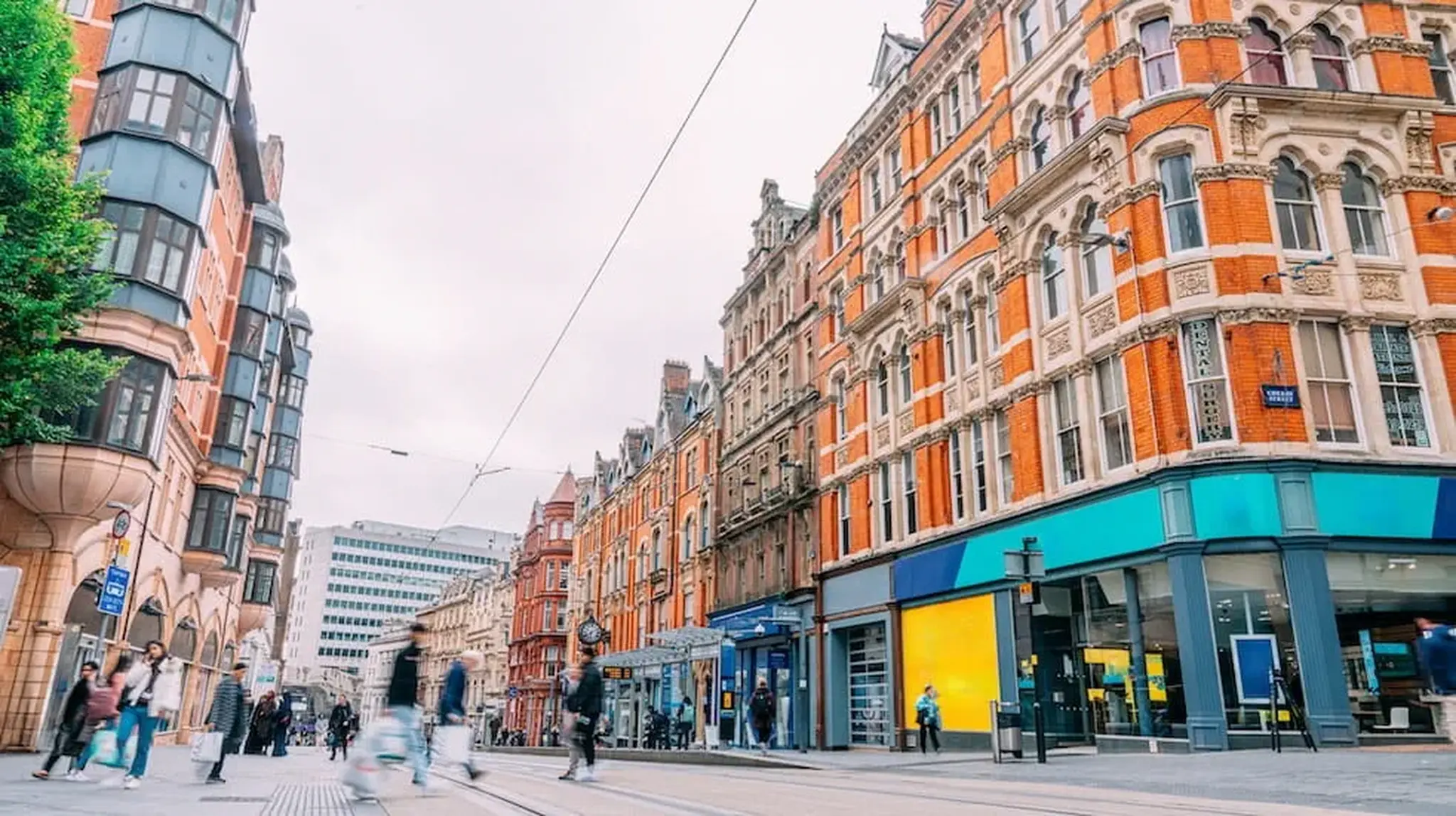 A bustling city street with red-brick Victorian buildings, shops, and pedestrians