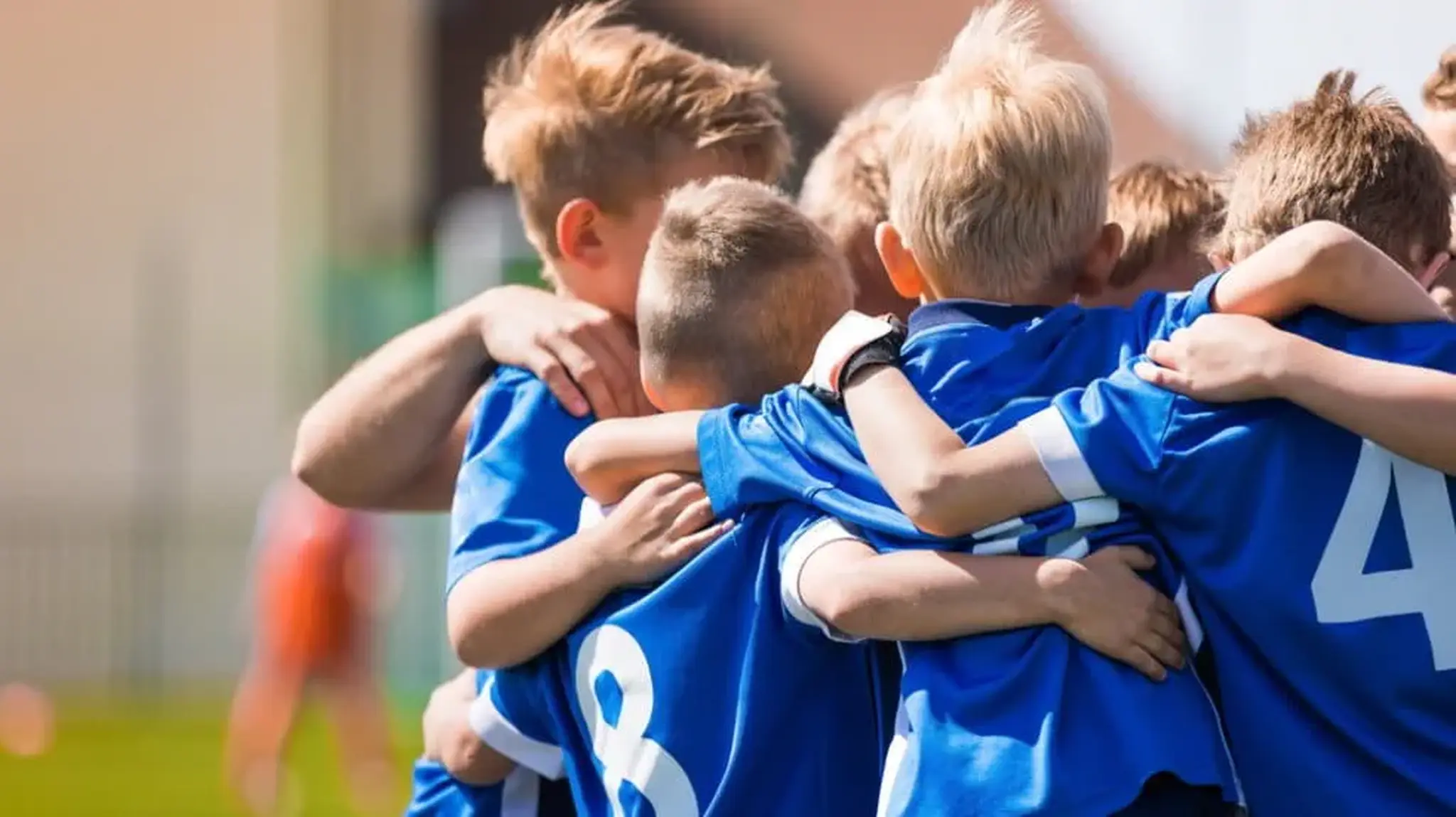 A group of young boys in blue jerseys huddle together in a circle