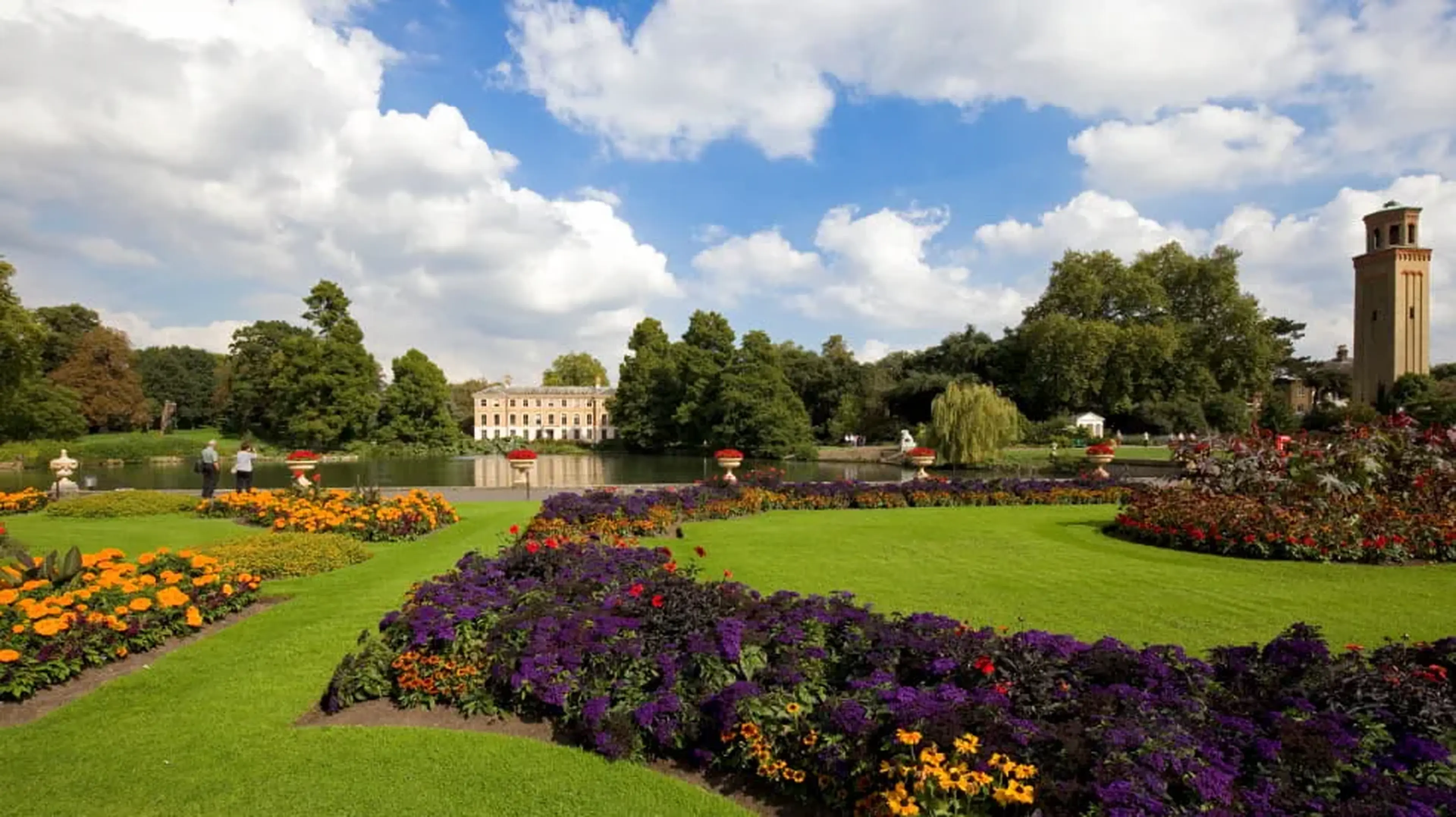 Beautiful Kew Gardens with vibrant flower beds, green lawn, and a historic building by a lake