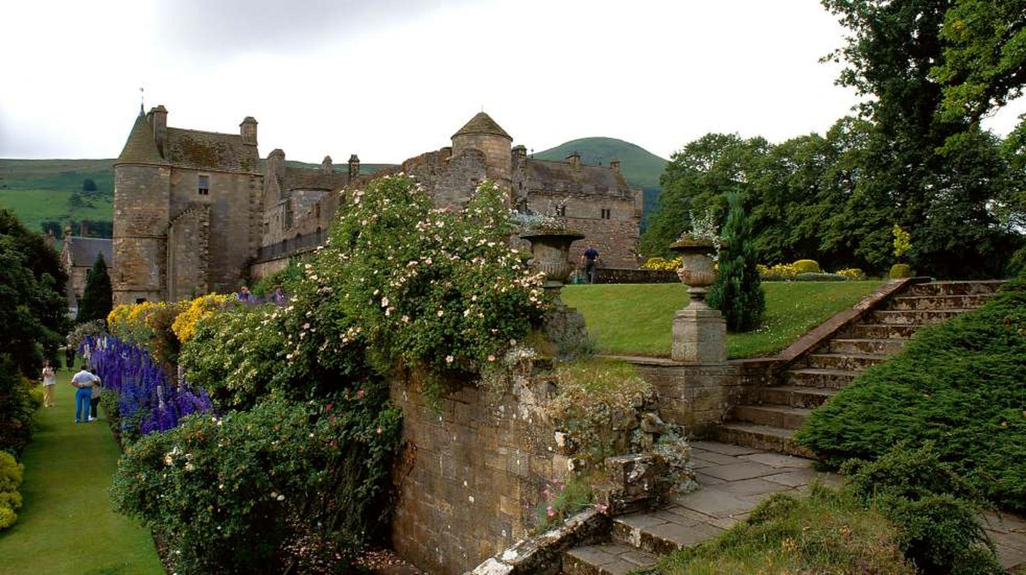 Historic stone castle with lush gardens, vibrant flowers, and large trees