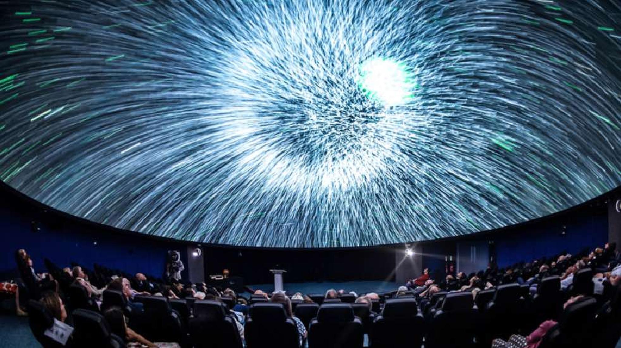 People seated in a planetarium observe a dynamic, starry display on the dome ceiling
