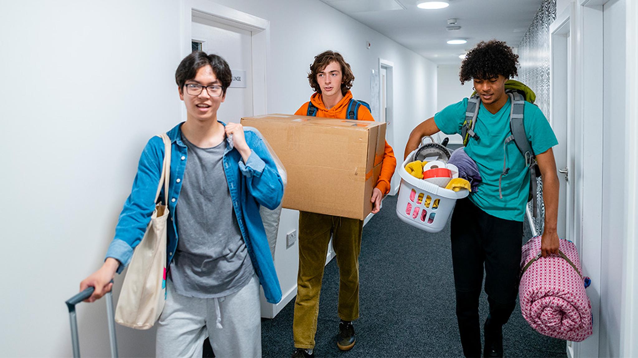 Three students carrying a suitcase, large box and laundry basket