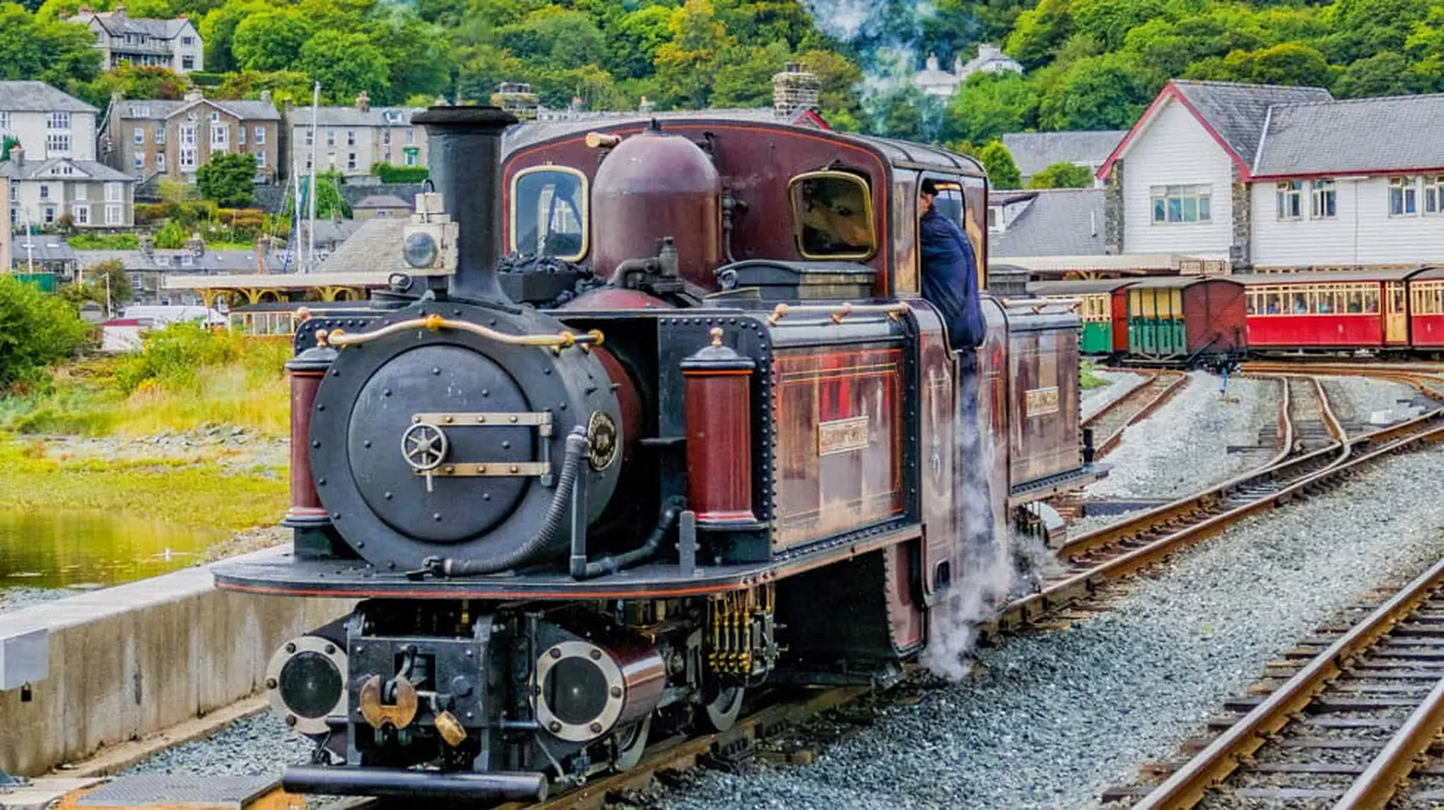 A vintage steam train with a maroon exterior emits steam