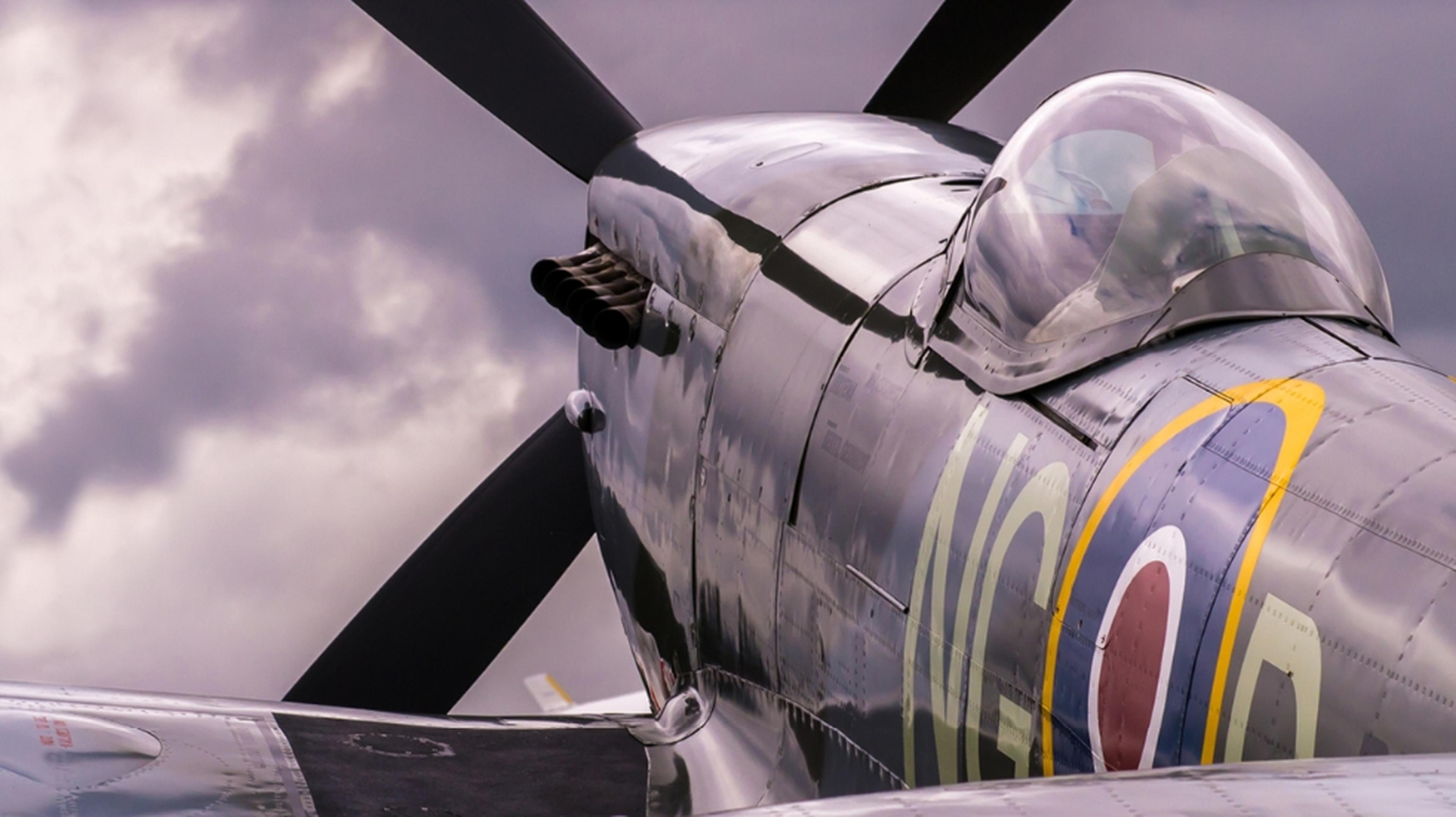 Close-up of a vintage fighter plane, featuring a propeller and cockpit. The aircraft has distinctive markings and is set against a cloudy sky.