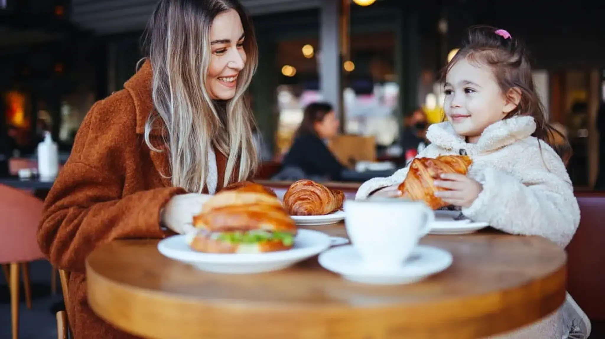 A woman and a little girl enjoying croissants and hot drink at an outdoor café