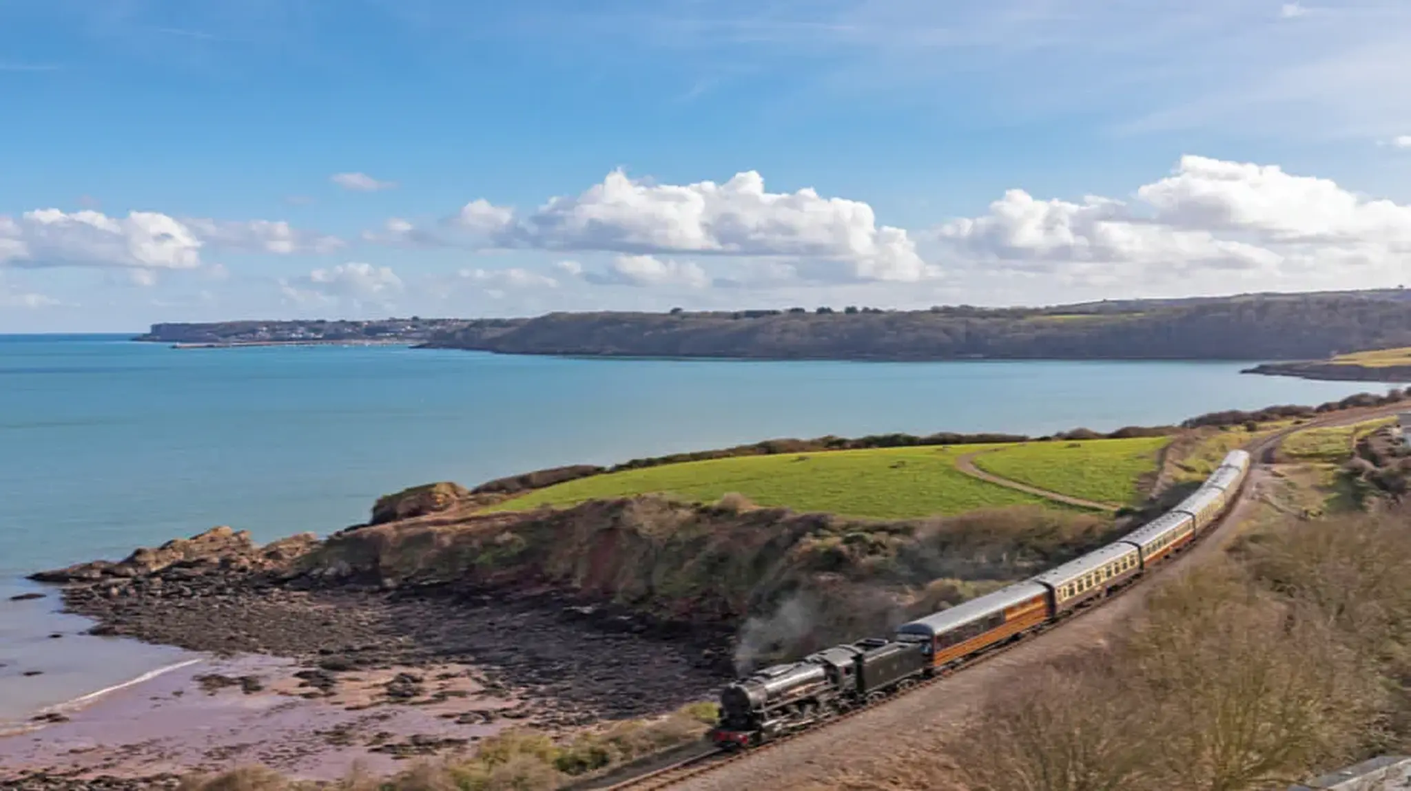 A steam train travels along a coastal track