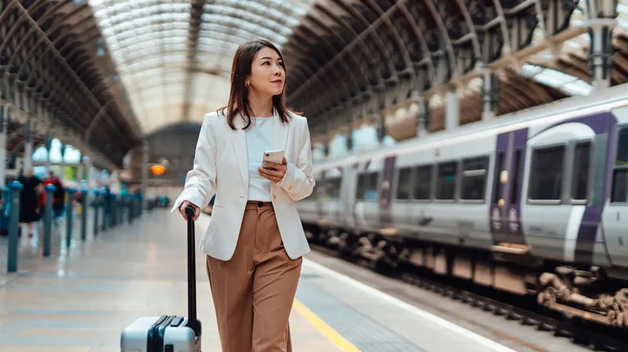 Woman walking with a suitcase and phone on a train platform