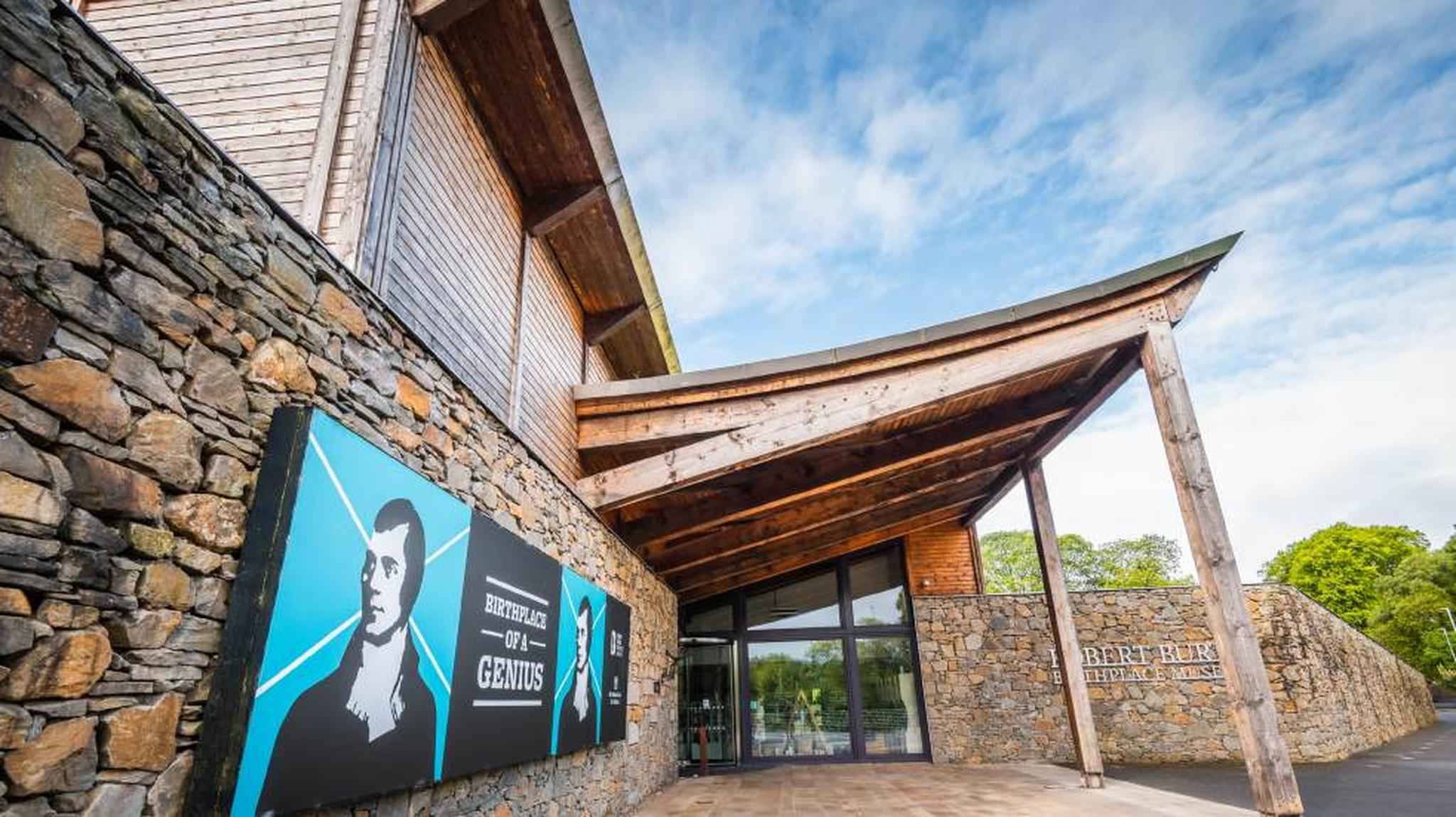 The entrance of a stone walled modern building, with a large sign depicting a black-and-white portrait of a person