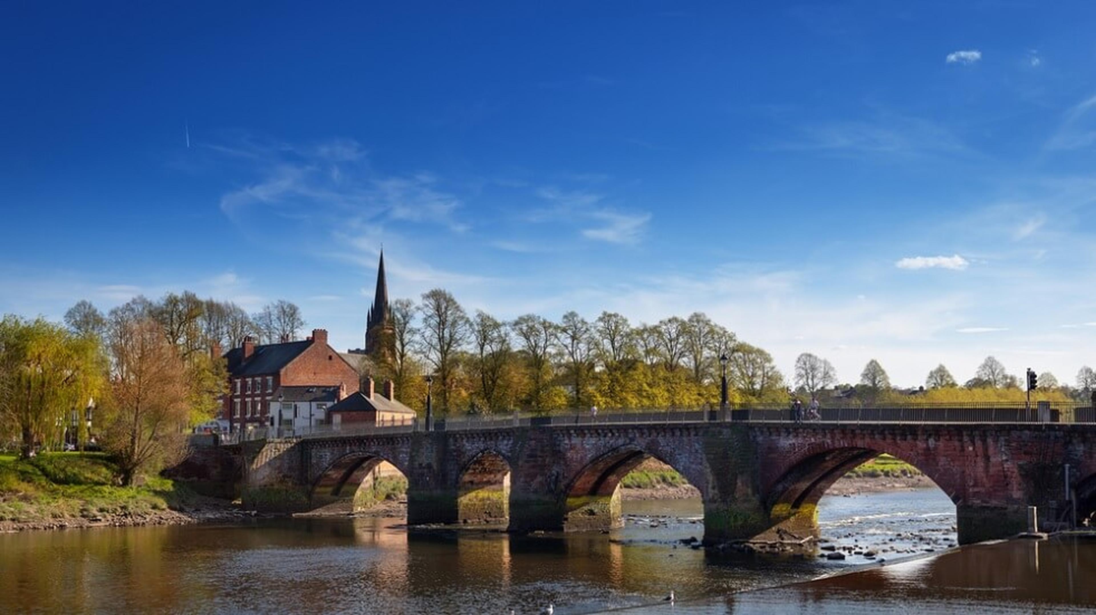 Stone bridge over a calm river, with historic buildings