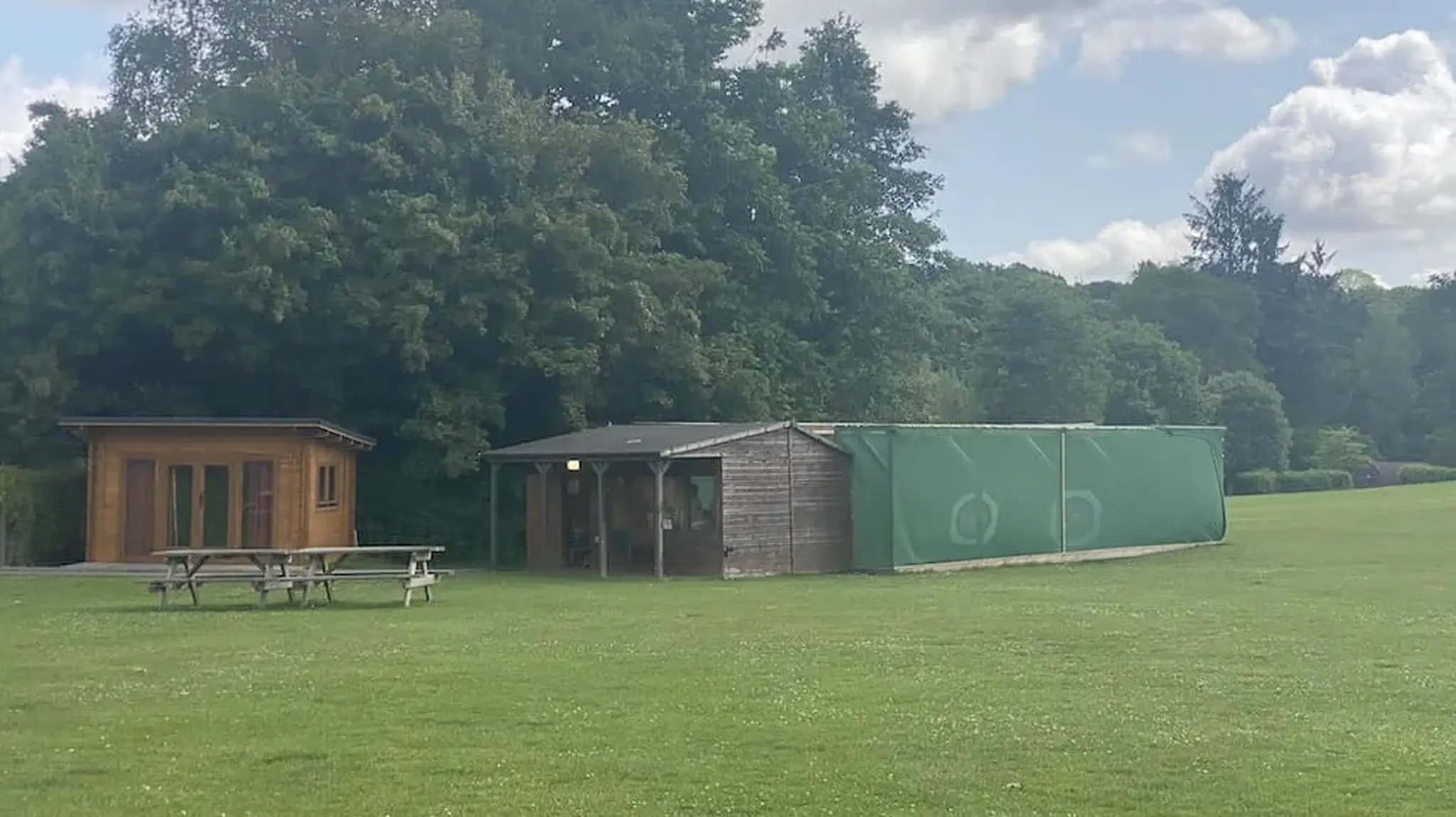 A wooden cabin and a structure with green netting on a grassy field