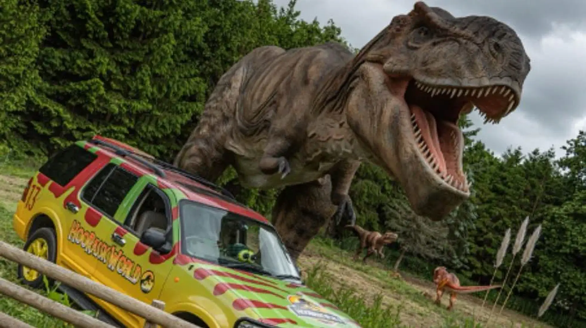 A large, roaring dinosaur model stands near a colourful off-road vehicle