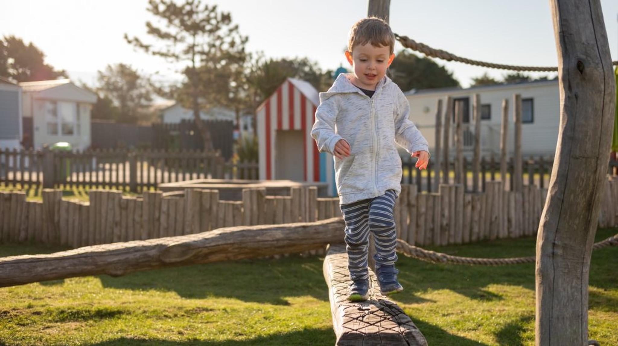 A young child balancing on a wooden beam at a playground
