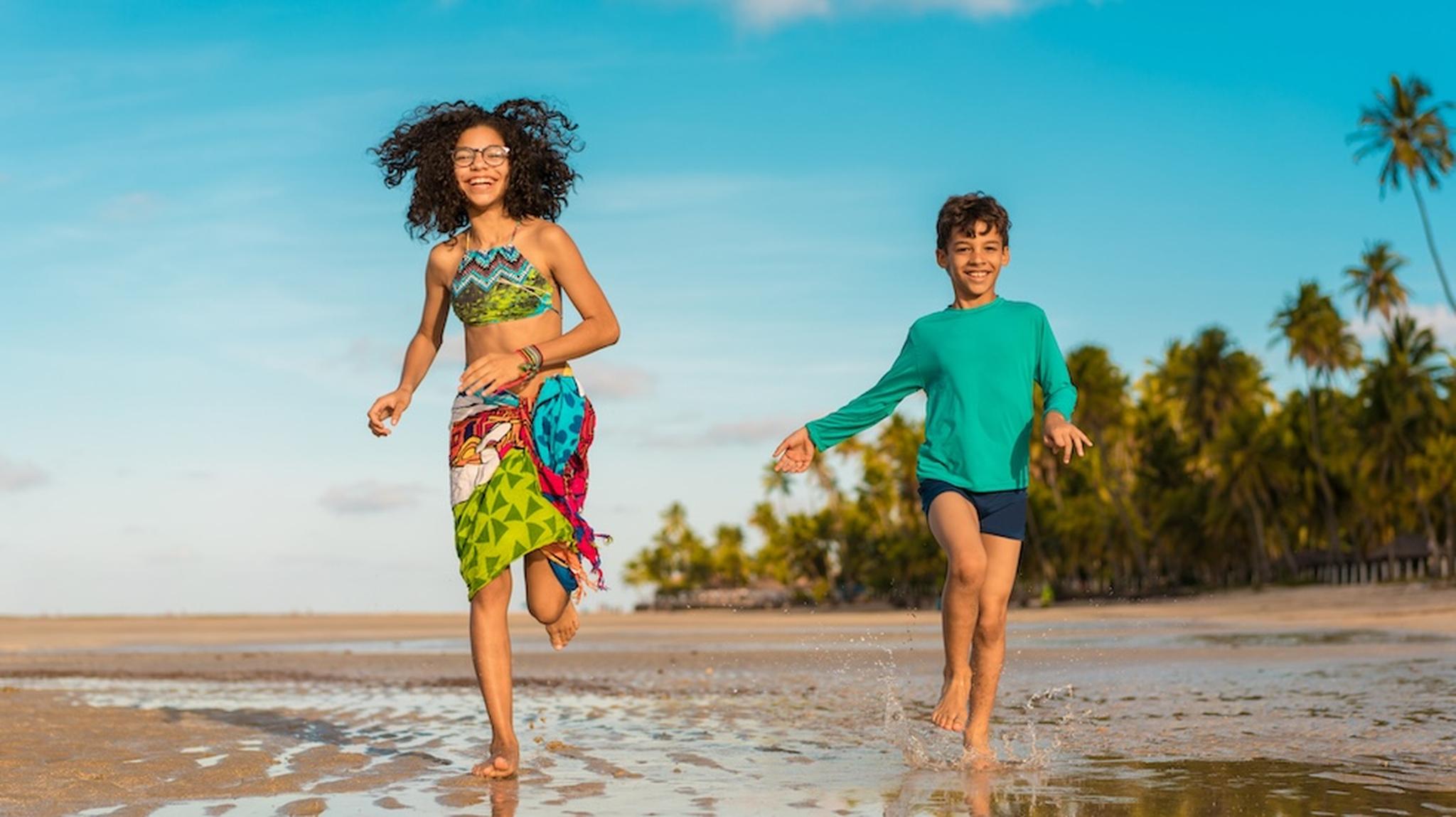 Girl and boy smiling and running on beach