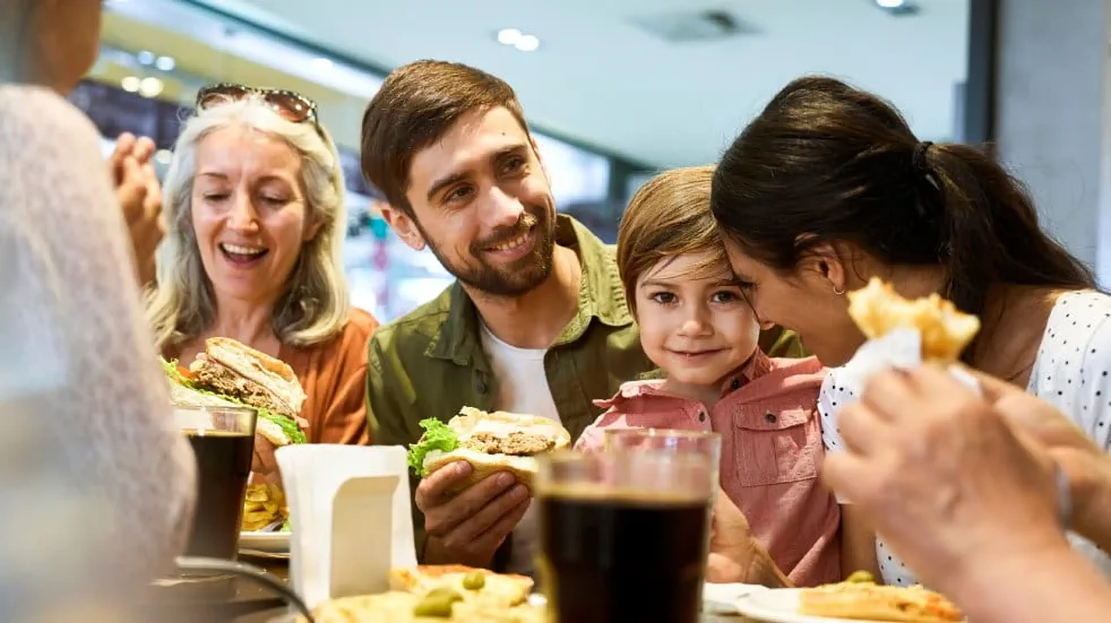 Family enjoying a meal together at a restaurant, with sandwiches and drinks