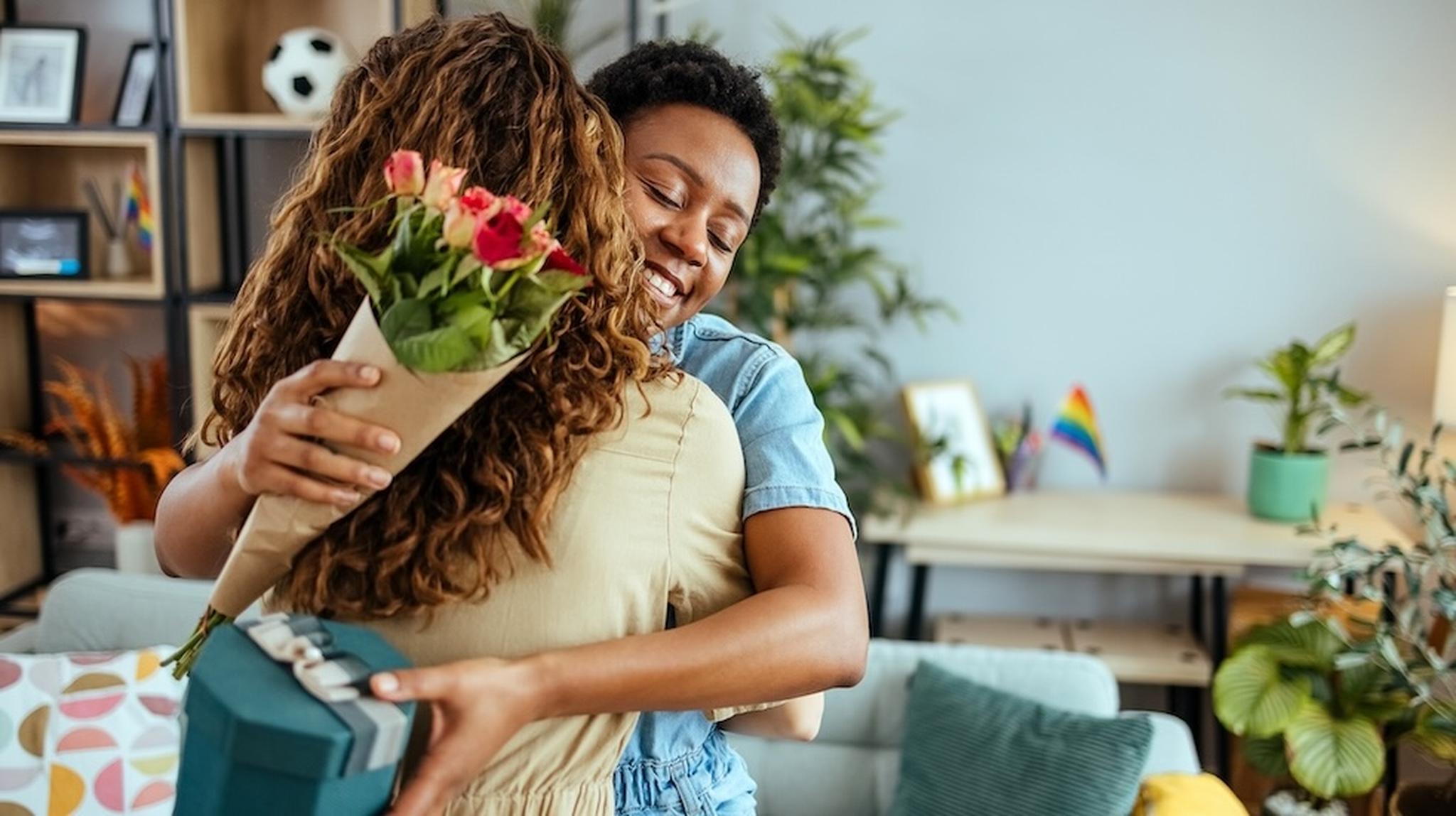 A lady hugging a lady holding flowers and gift box