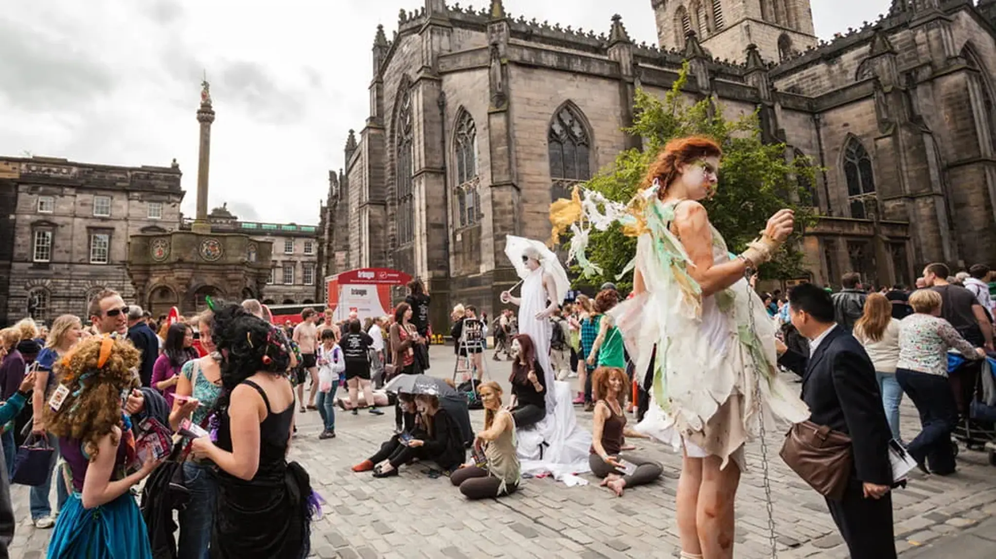 Street performers and crowds gather near a historic stone building, amidst festival