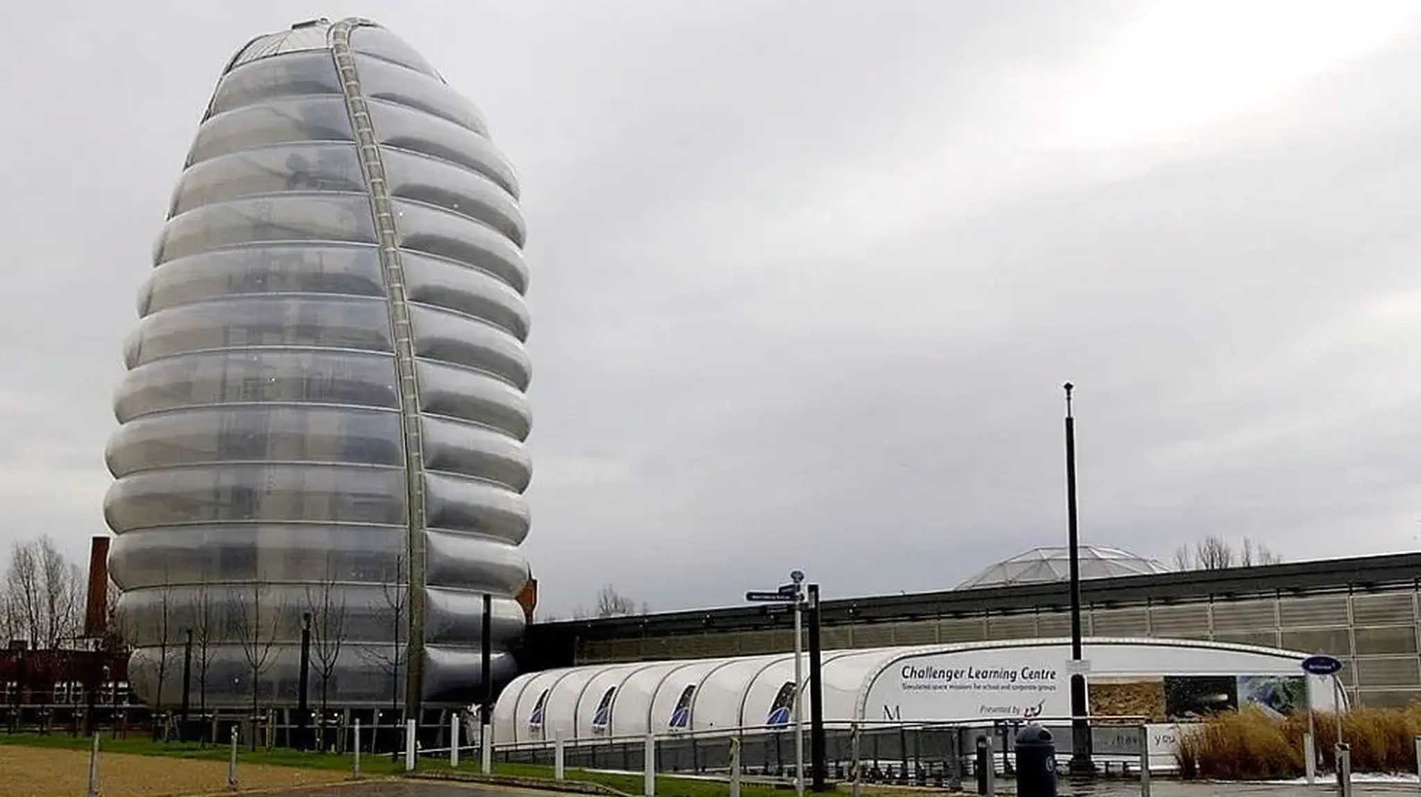 Futuristic silver building with a curved, ribbed design beside a low, modern structure