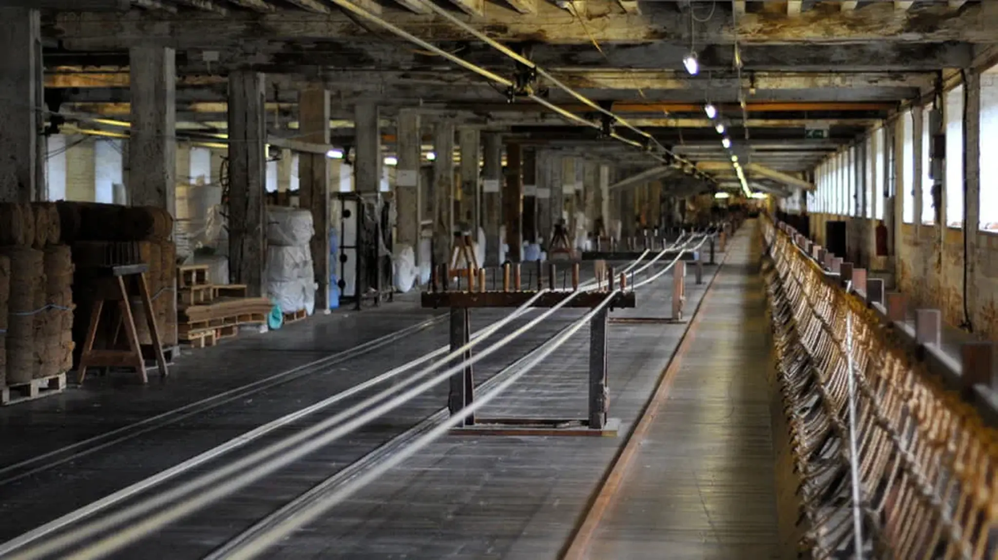 An interior of an old, empty textile mill with rows of spinning machines and wooden beams