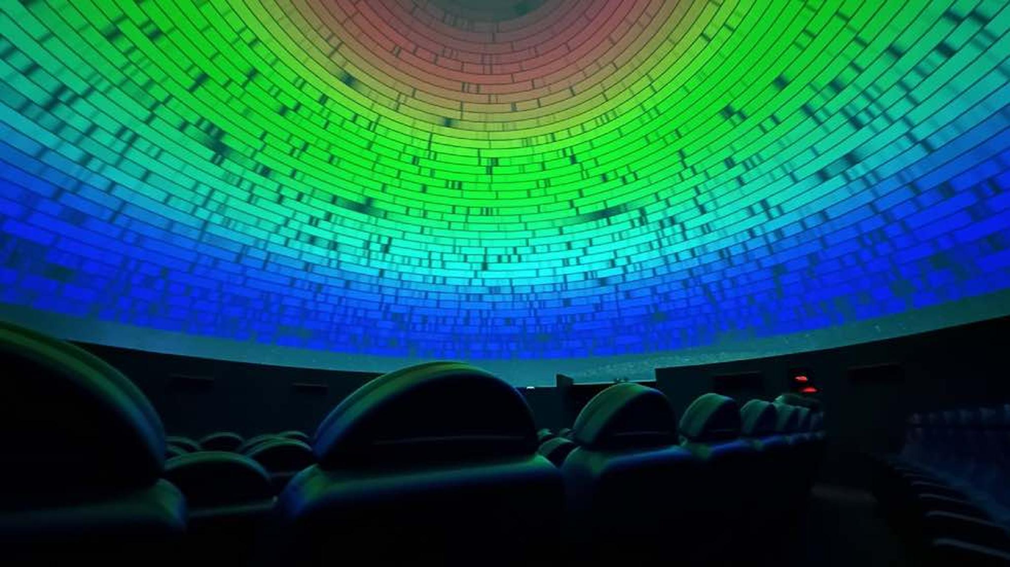 A planetarium dome with rows of seats, displaying a colourful gradient from green to blue