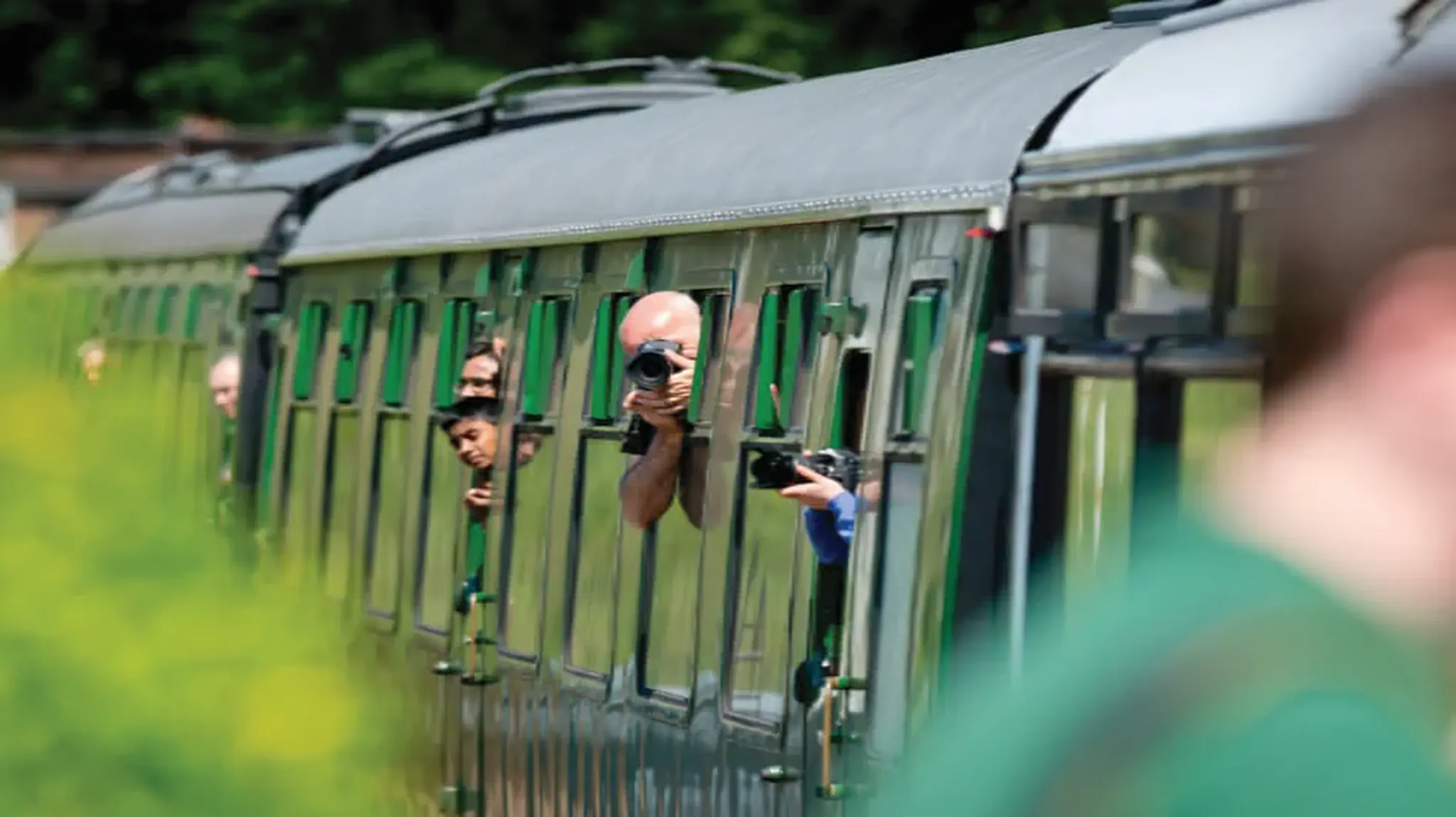 Passengers lean out of a moving train with cameras, capturing photos through the windows