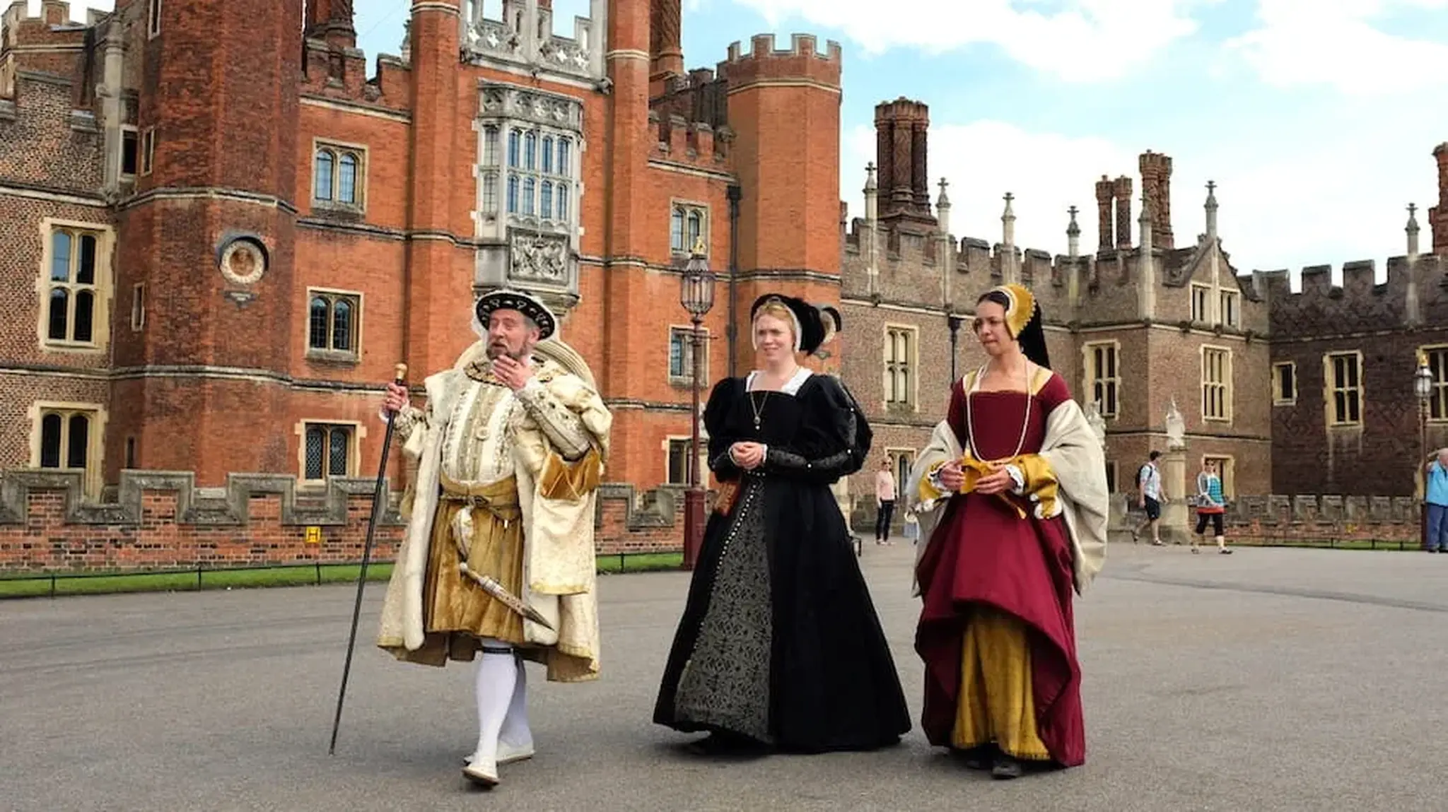 Three actors in front of Hampton Court Palace, dressed up in traditional Tudor costumes as historical figures
