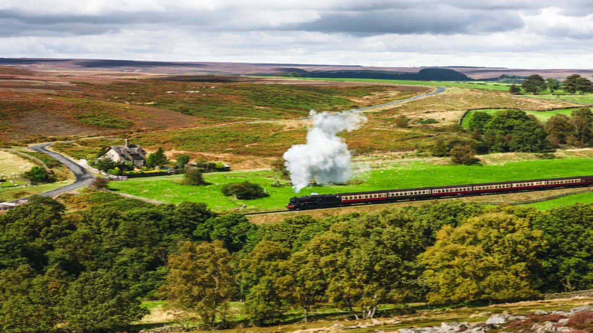 A steam train travels through green countryside with rolling hills