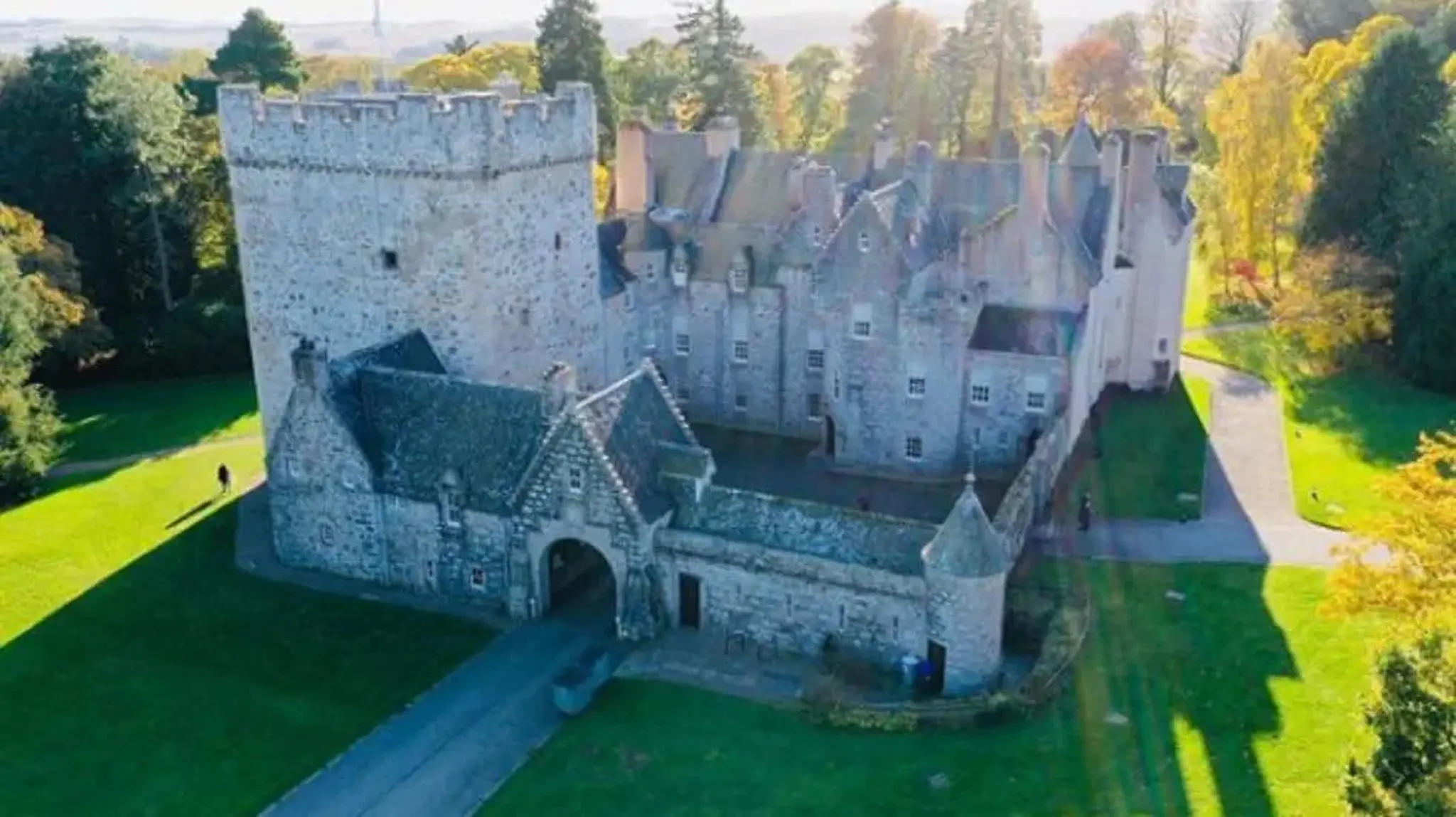 Aerial view of a historic stone Drum Castle surrounded by green lawns and trees