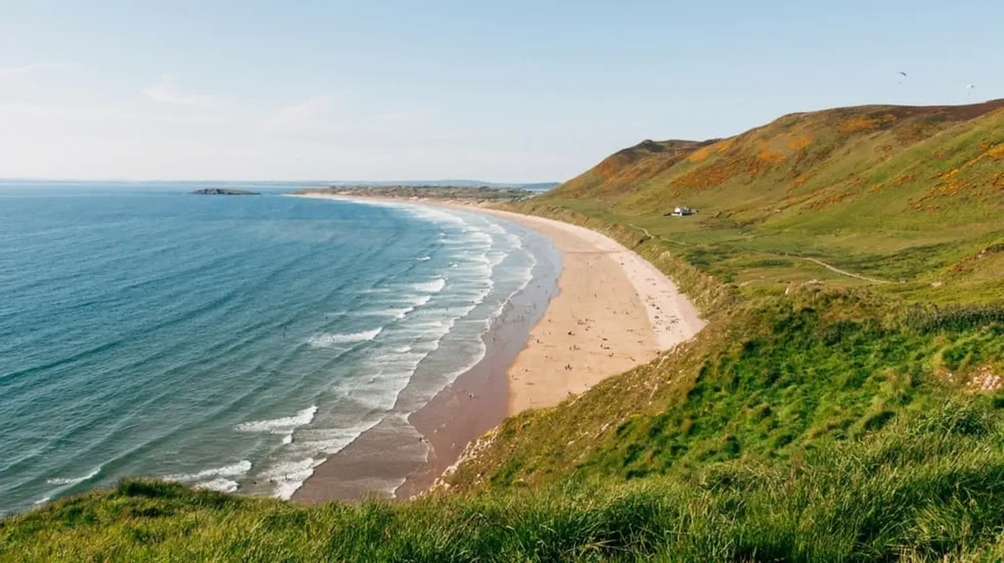 A scenic coastal view of Rhossili Bay, showcasing a curving sandy beach
