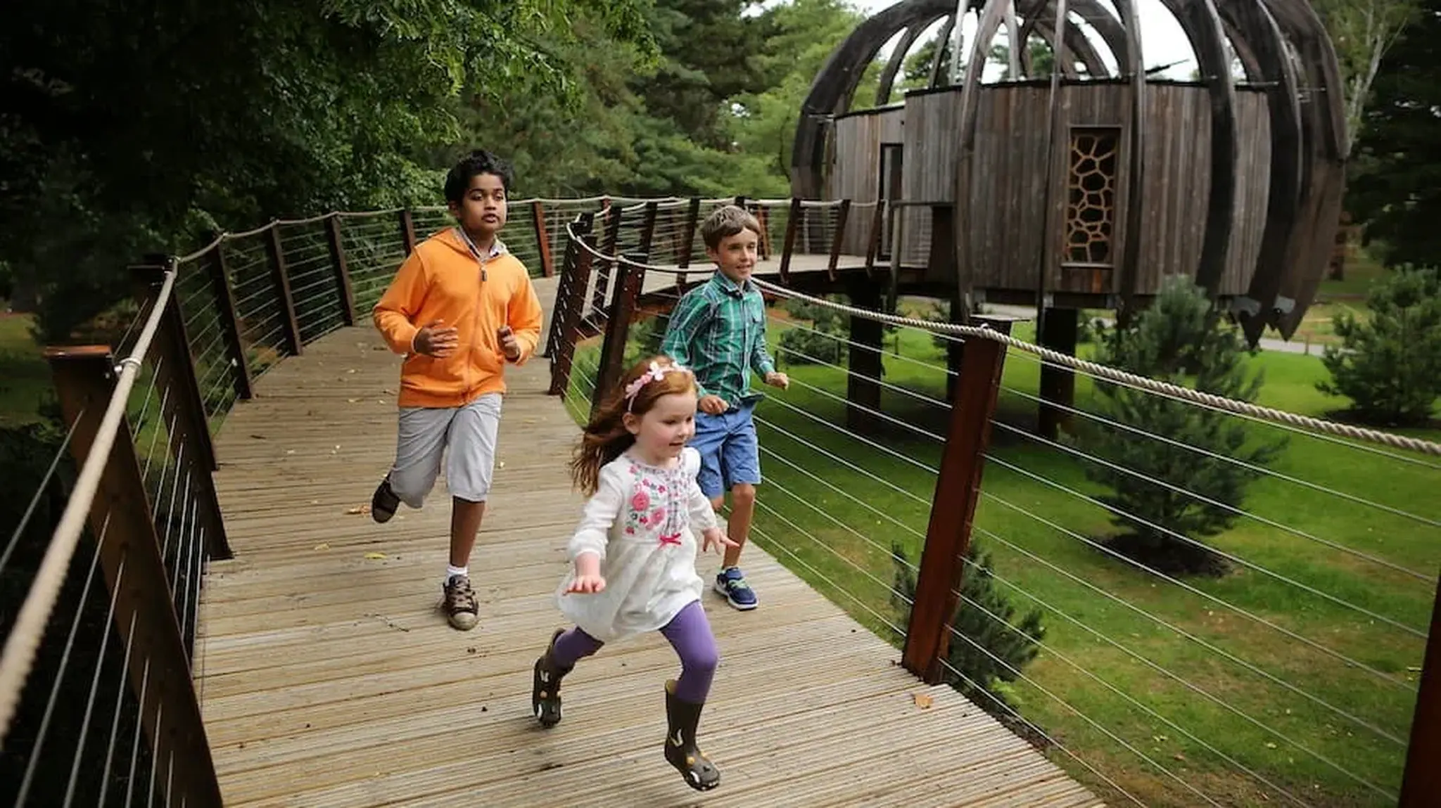 Three children running on a wooden walkway in a park
