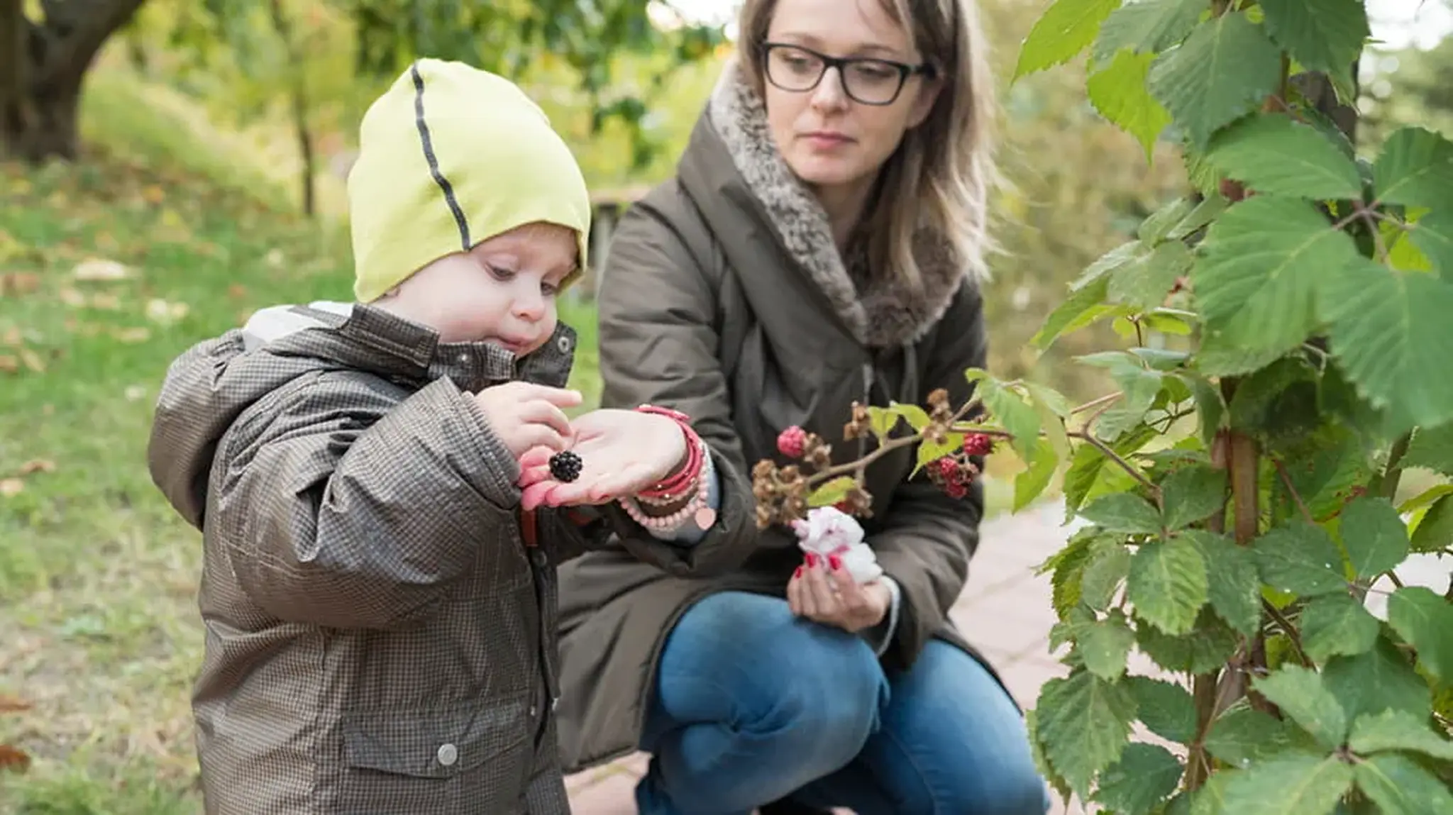 A woman offers berries to a child in a park