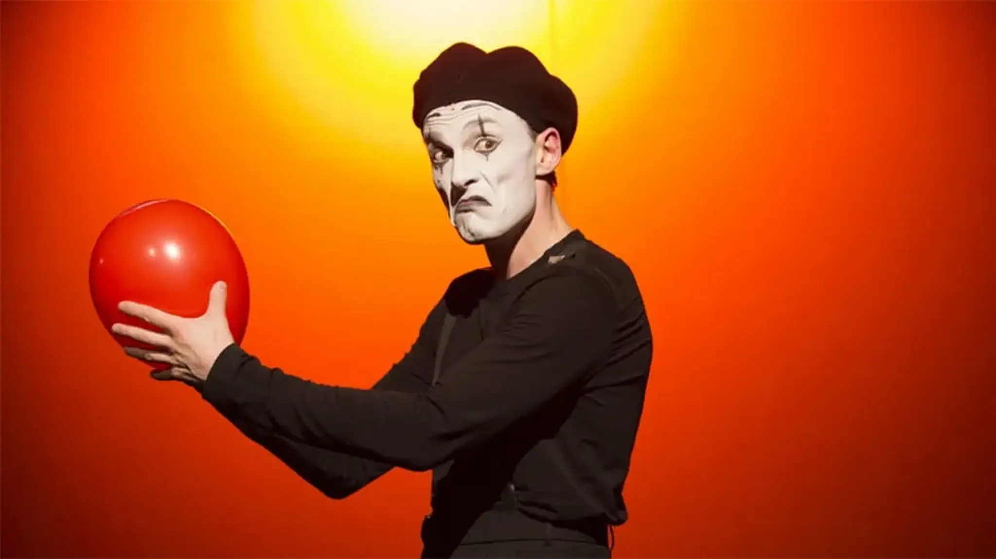Mime in black attire and white face paint holding a red balloon