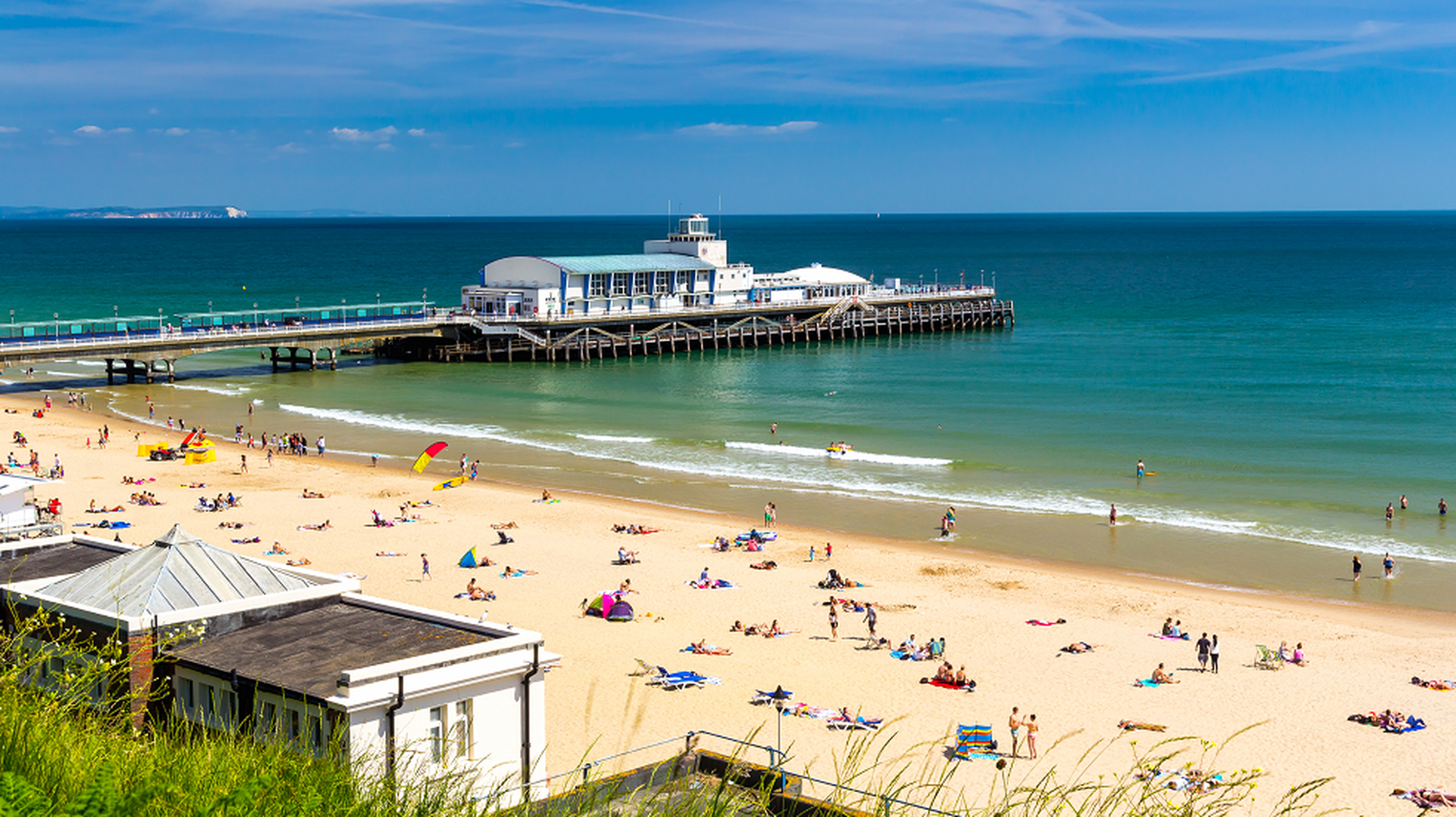 Sunny beach scene with people lounging and swimming near a pier