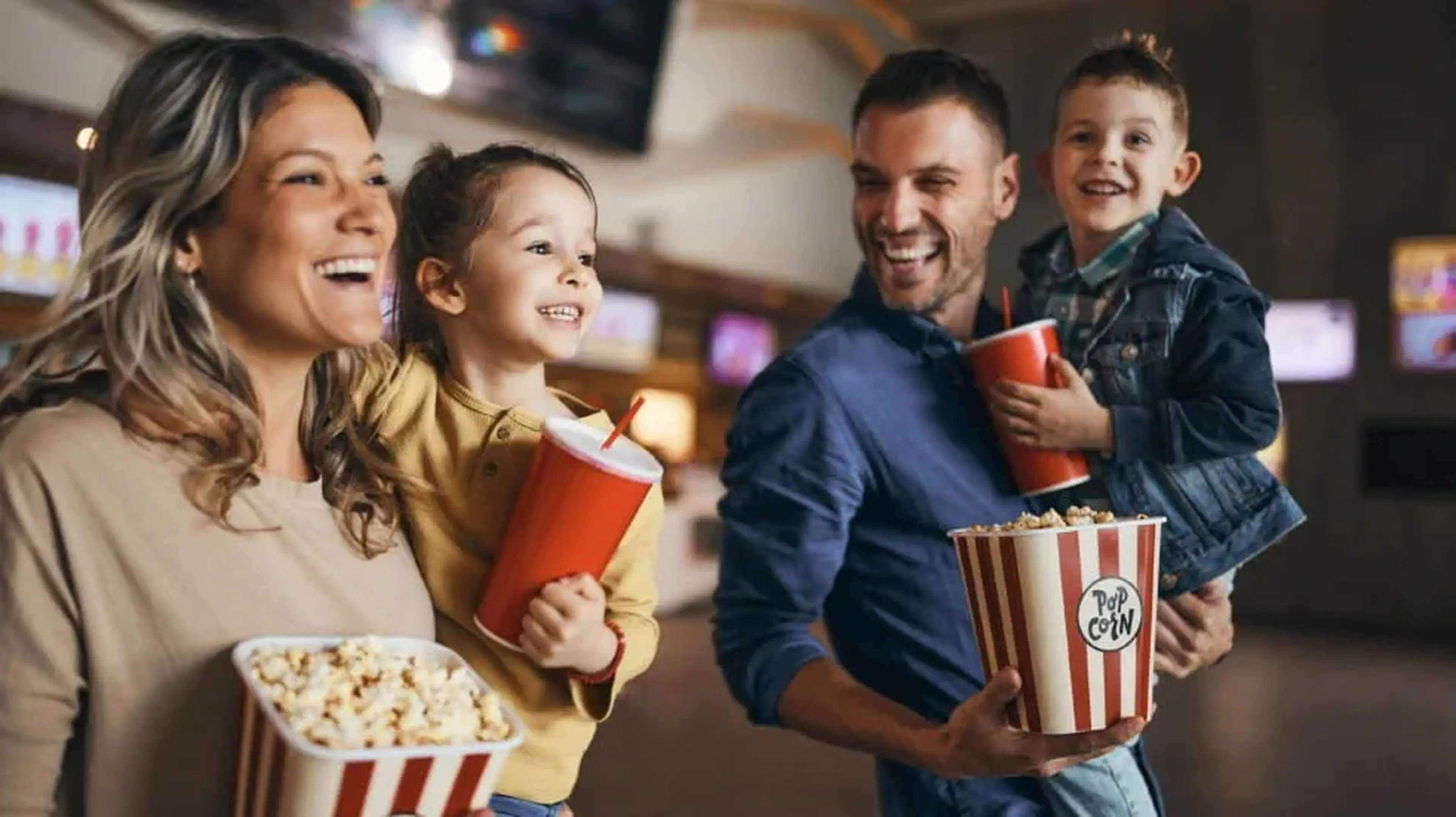 Happy family with two children holding popcorn and drinks in a cinema lobby.