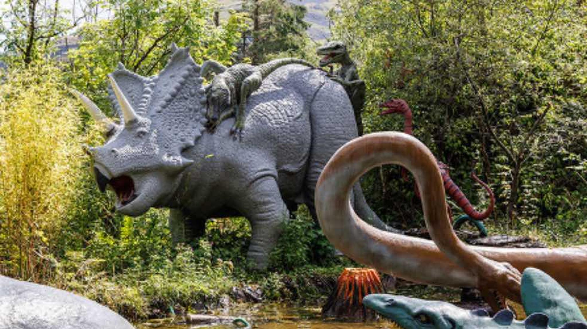 Several dinosaur statues, including a Triceratops and velociraptors, in a outdoor exhibit