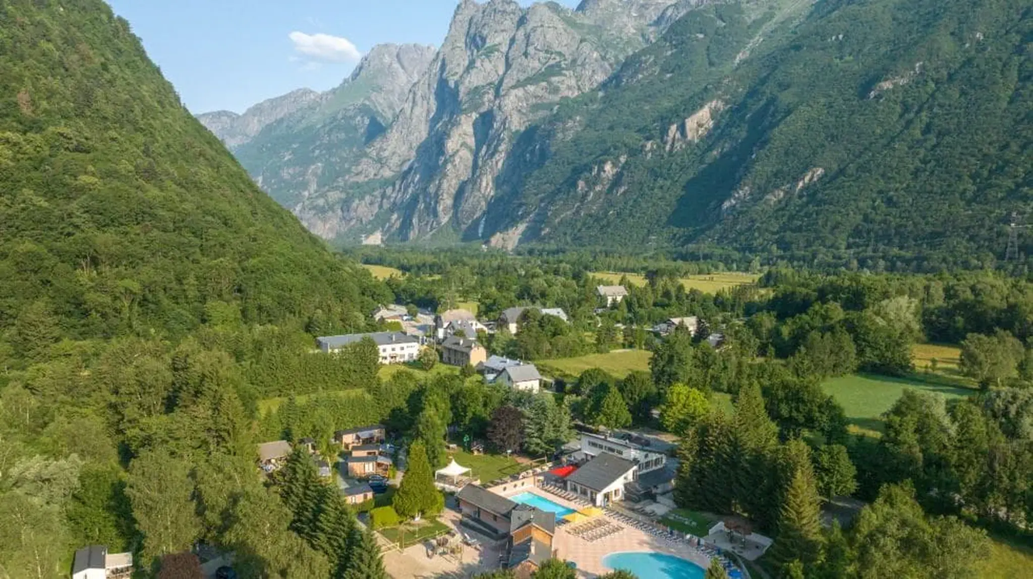 Aerial view of a green valley with scattered houses, a swimming pool, and mountains