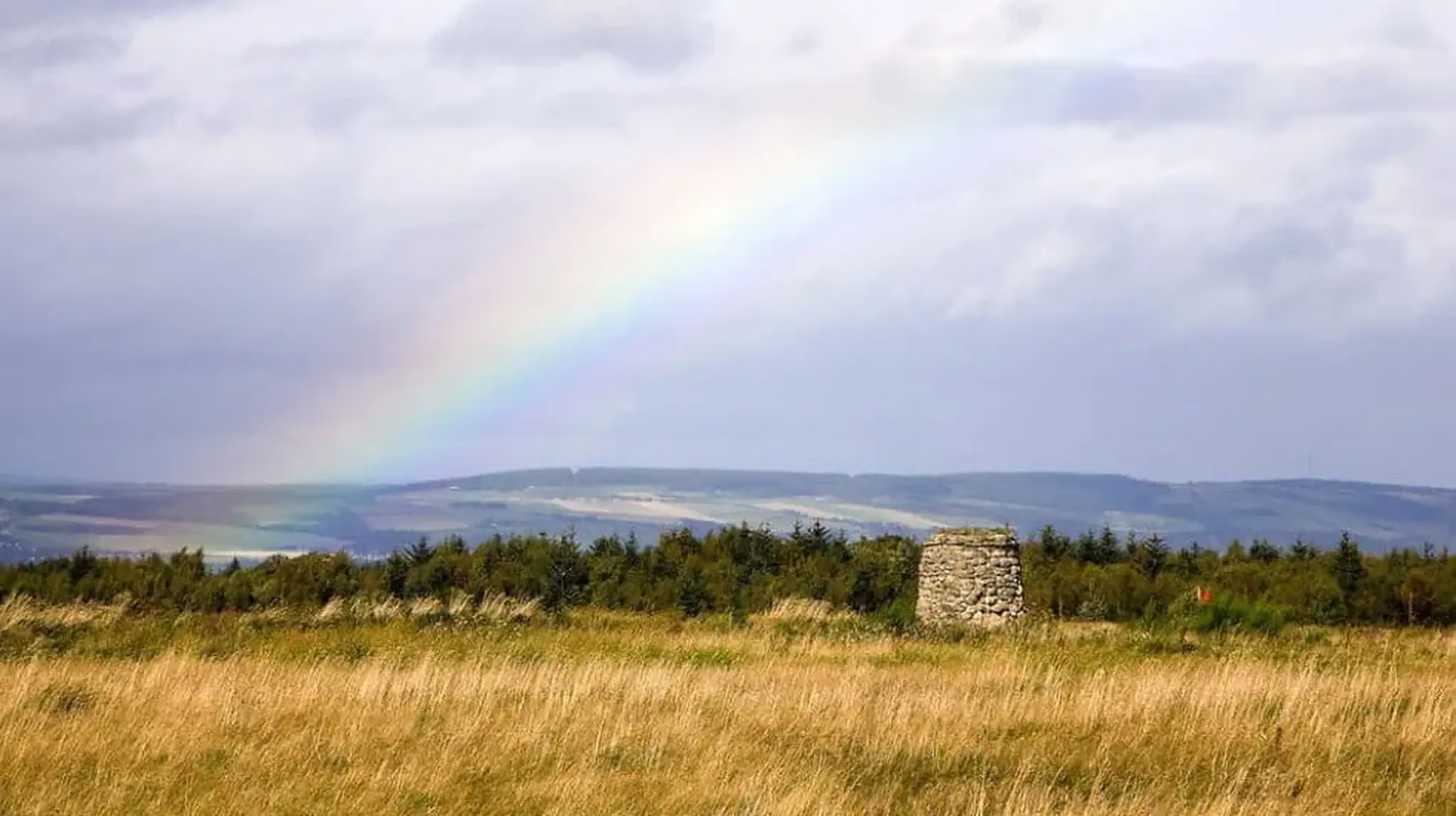 A rainbow arcs over a vast landscape of grassy fields