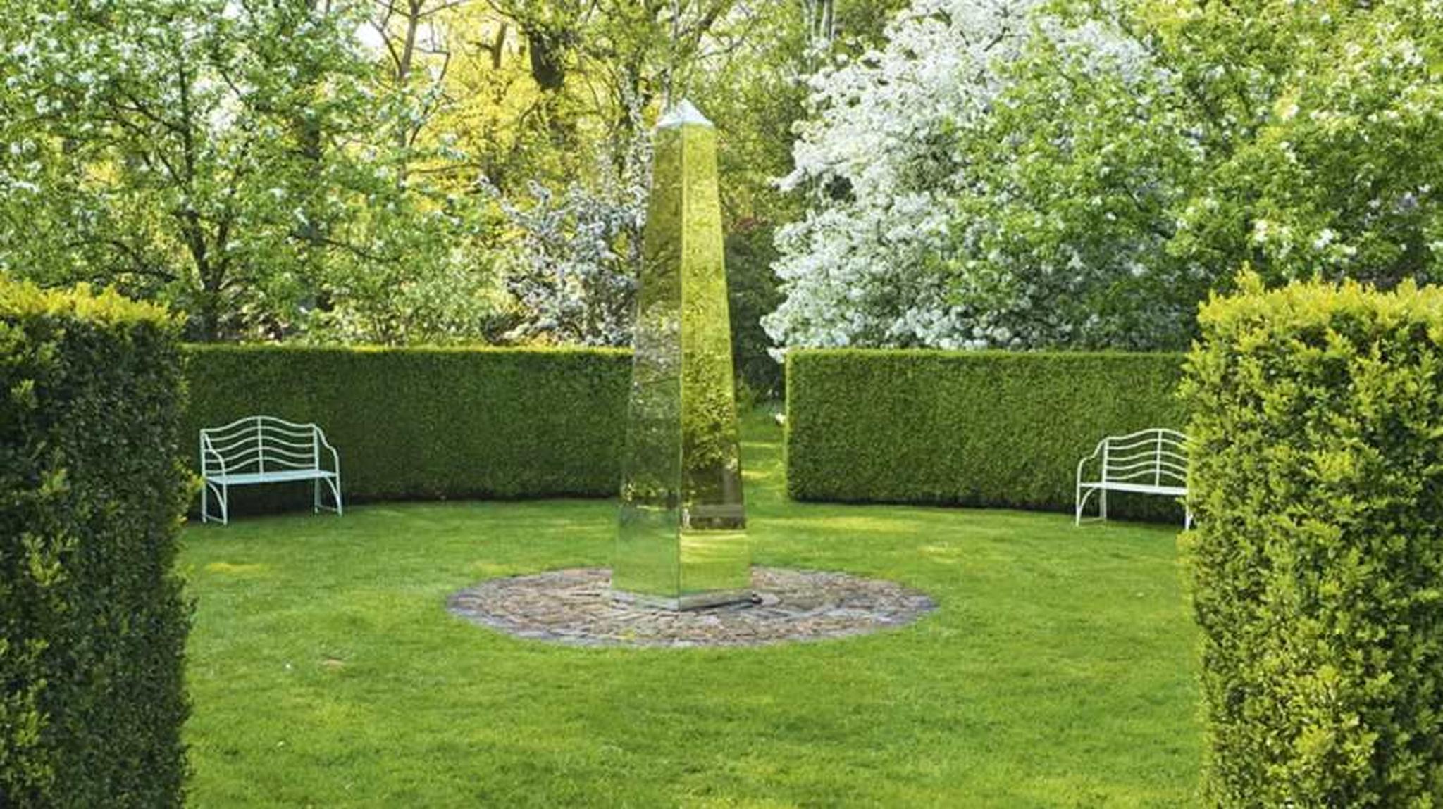 A reflective obelisk stands in the centre of Doddington Place Gardens with green hedges