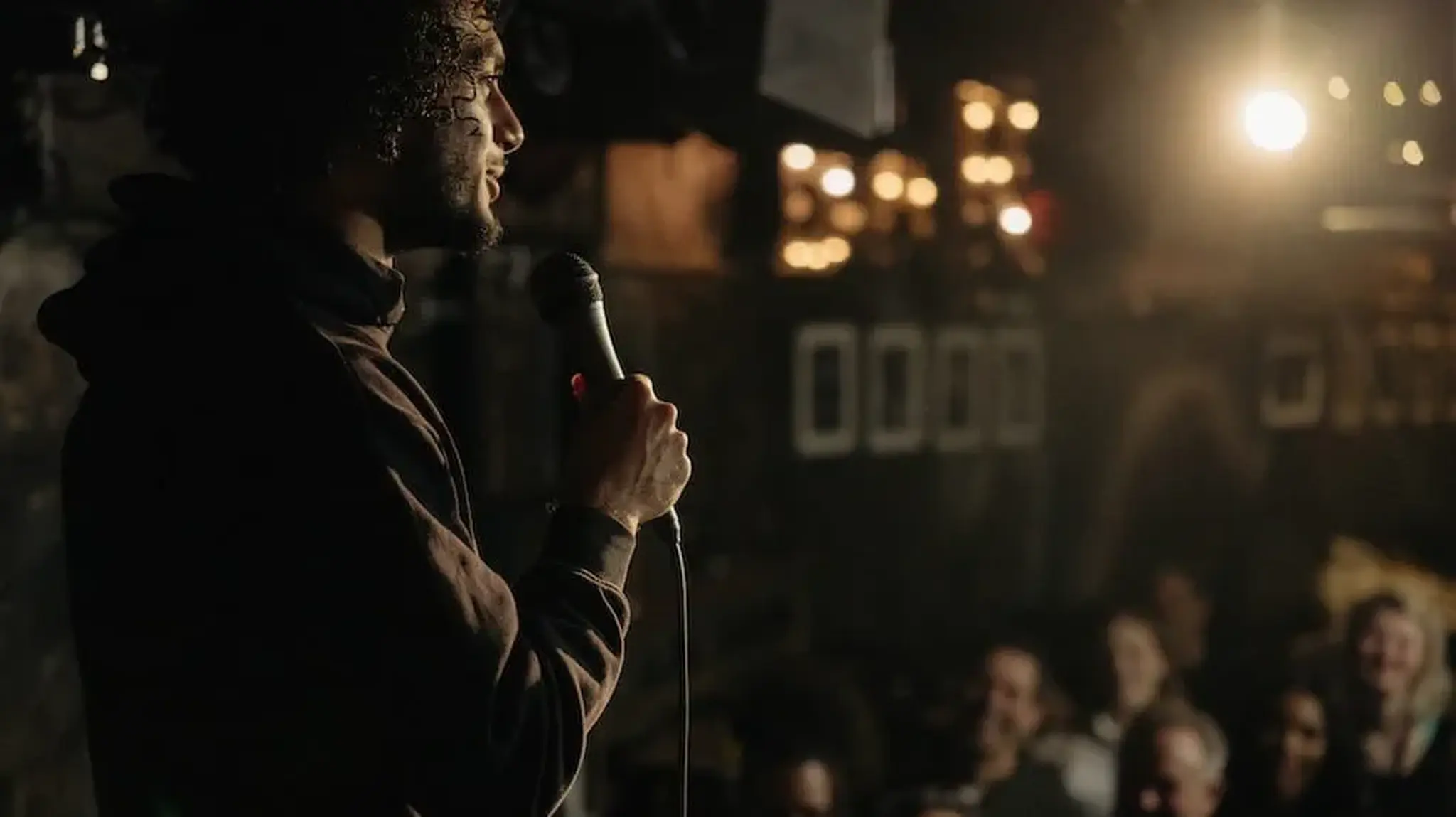 A comedian performs on stage holding a microphone, with an audience