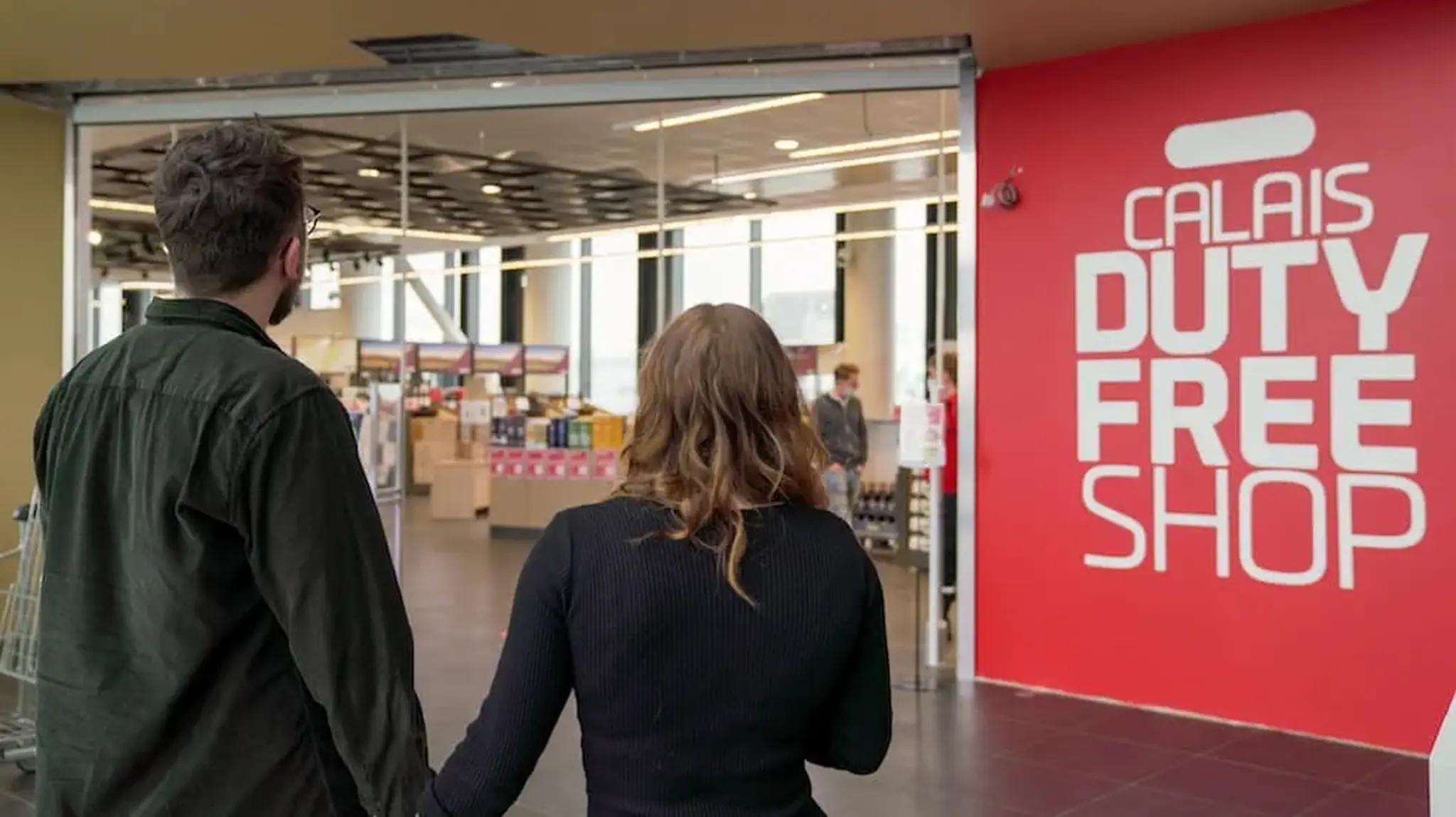 A couple holding hands approaches the entrance of Calais Duty Free Shop