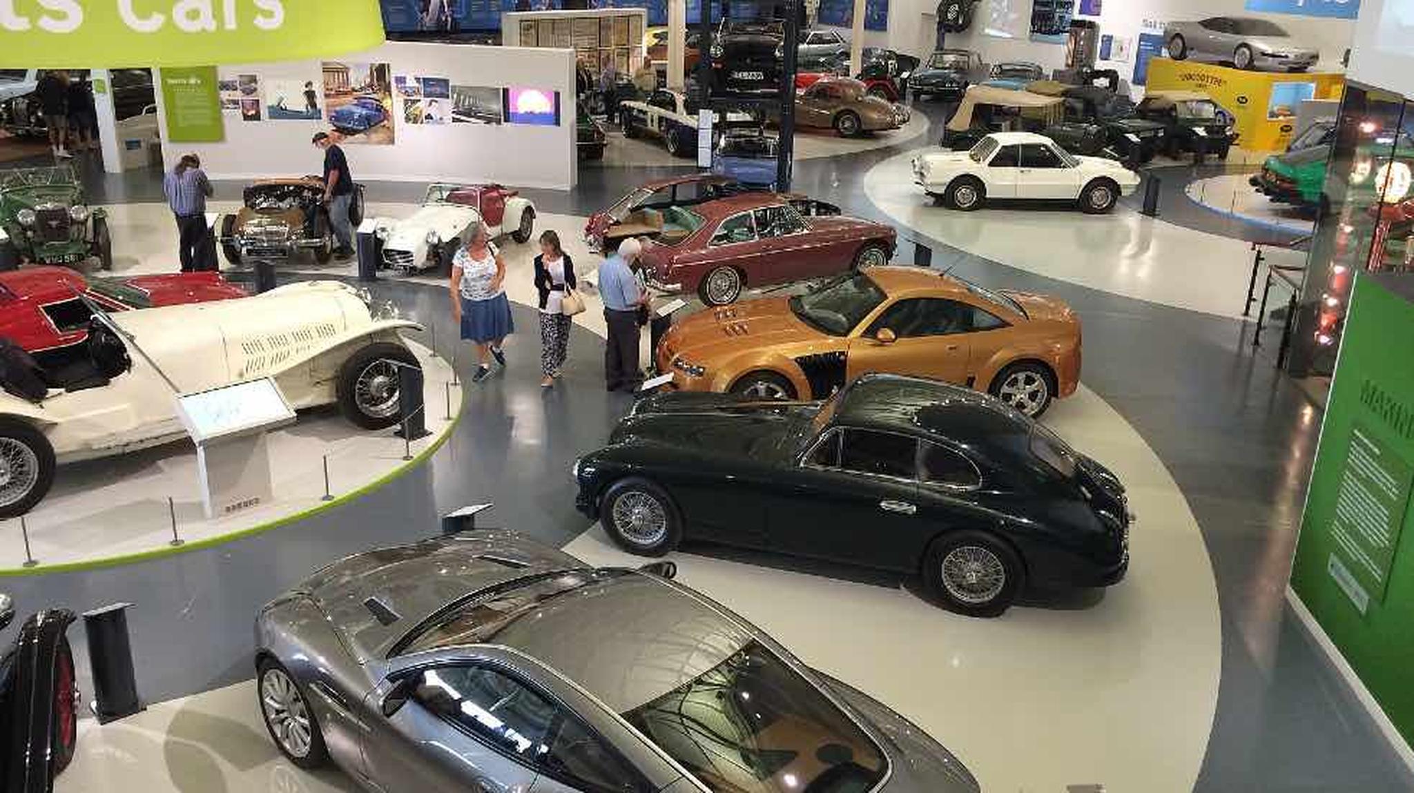People explore a car museum, featuring classic and modern vehicles displayed in the British Motor Museum