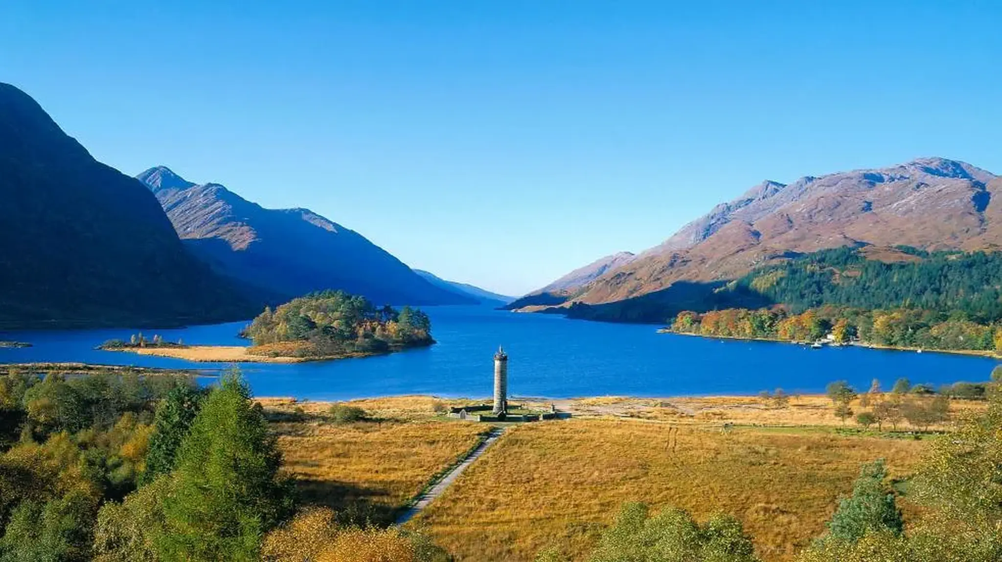 A scenic view of Glenfinnan Monument by a blue lake, surrounded by mountains