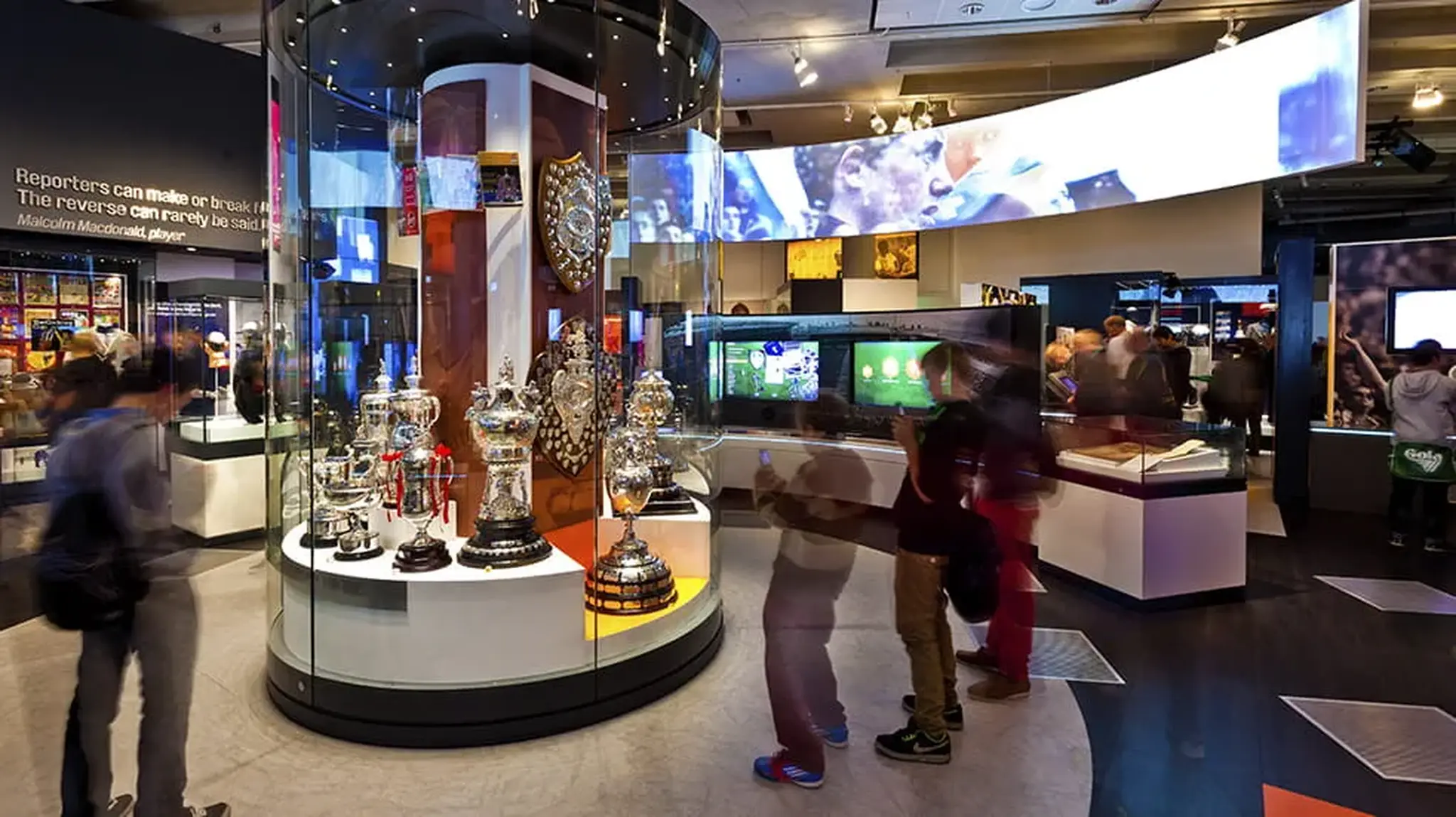 Visitors browse a museum exhibit featuring a collection of sports trophies