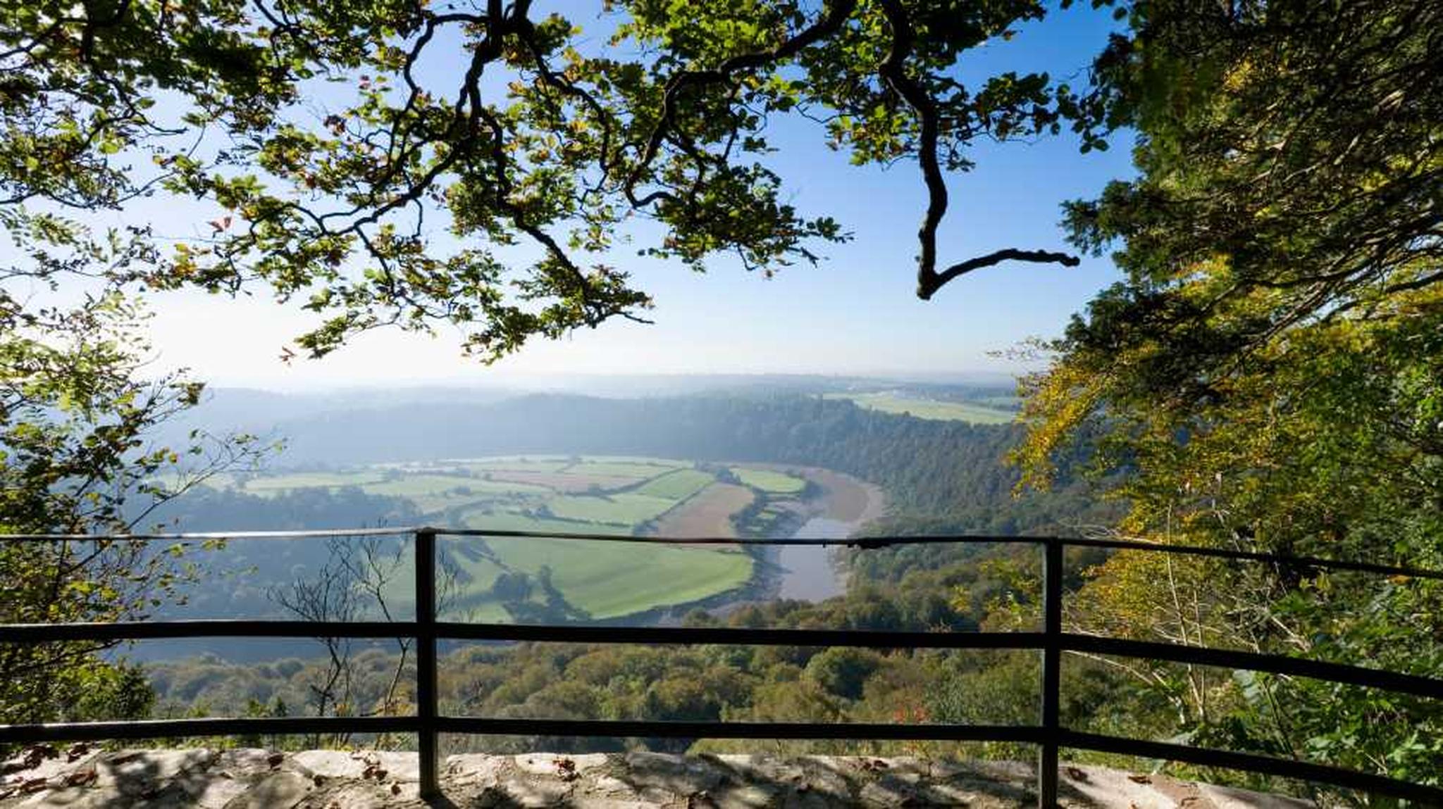 A scenic view from a stone ledge with a railing and overlooking a winding river
