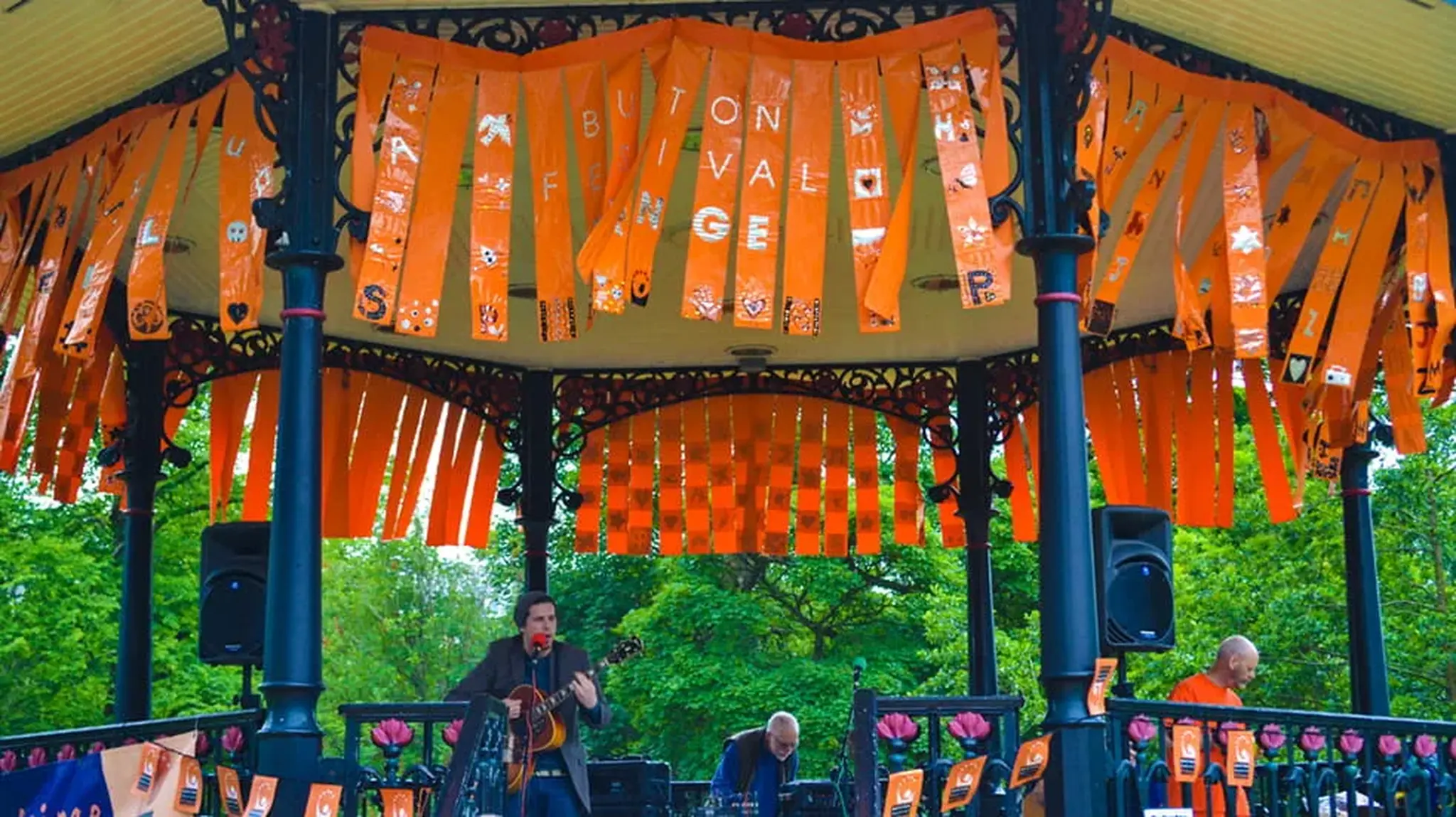 A band performs in a gazebo adorned with orange banners