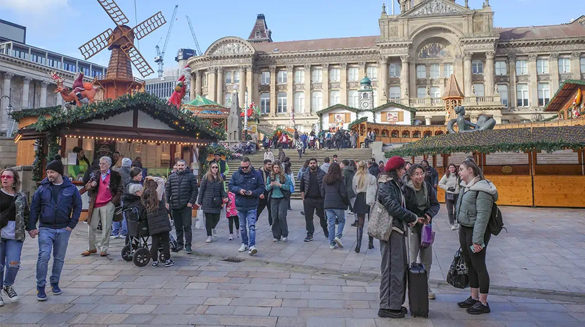 People walk through a festive outdoor marketplace with wooden stalls