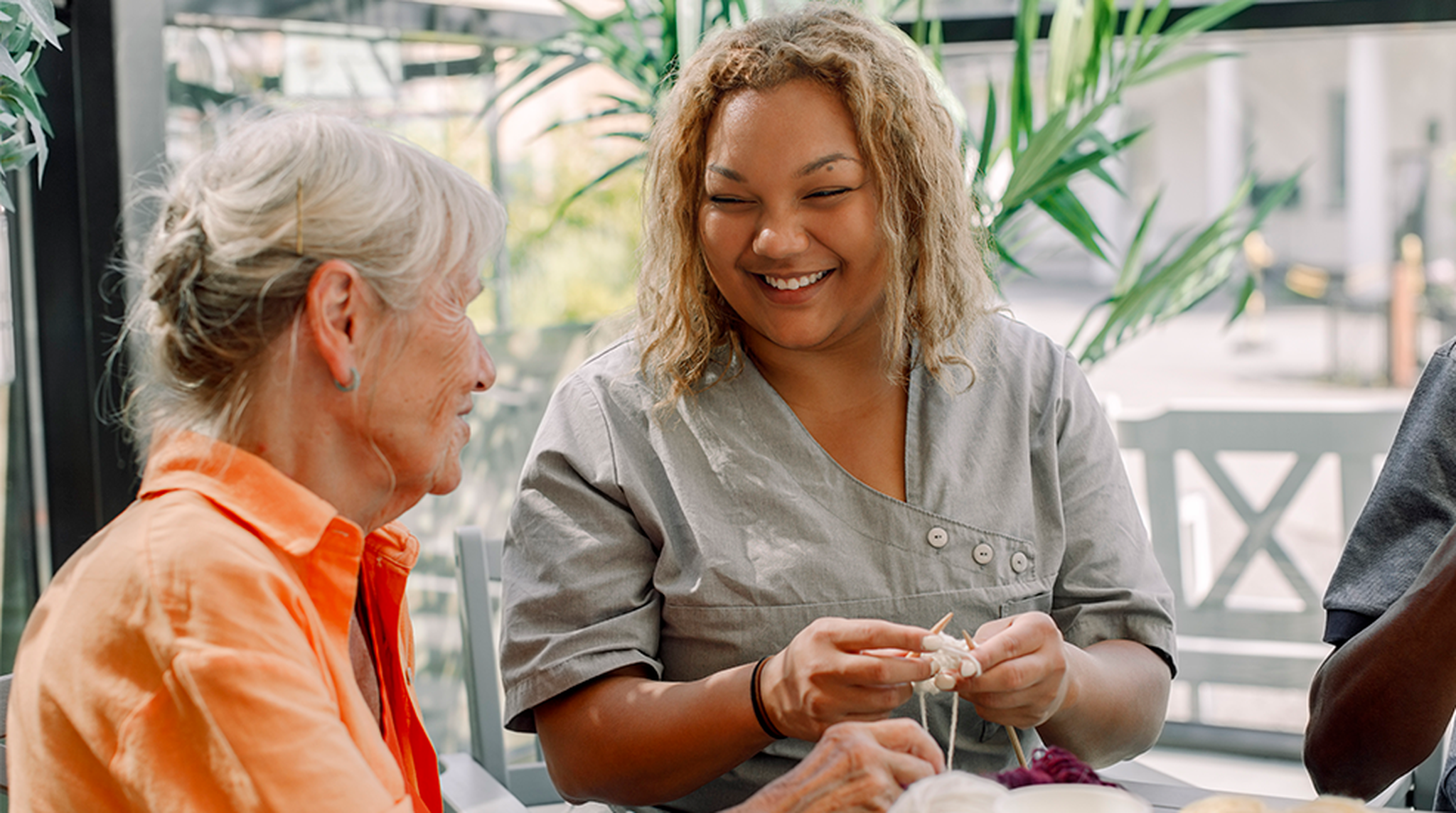 Happy young female caregiver crocheting with senior woman and man at retirement home